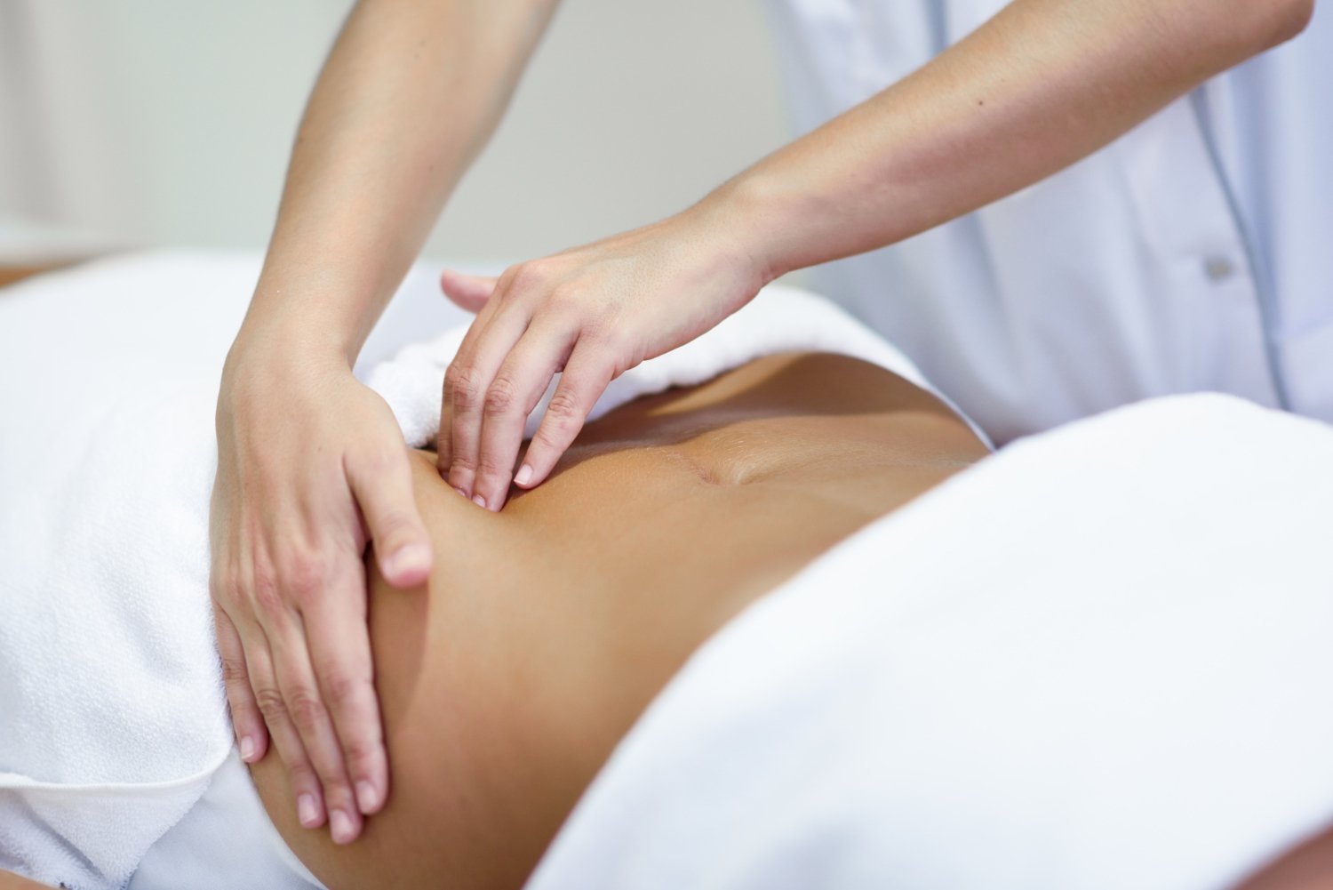 Women laying down on a therapy bed wrapped around in a towel with therapist massaging colon.