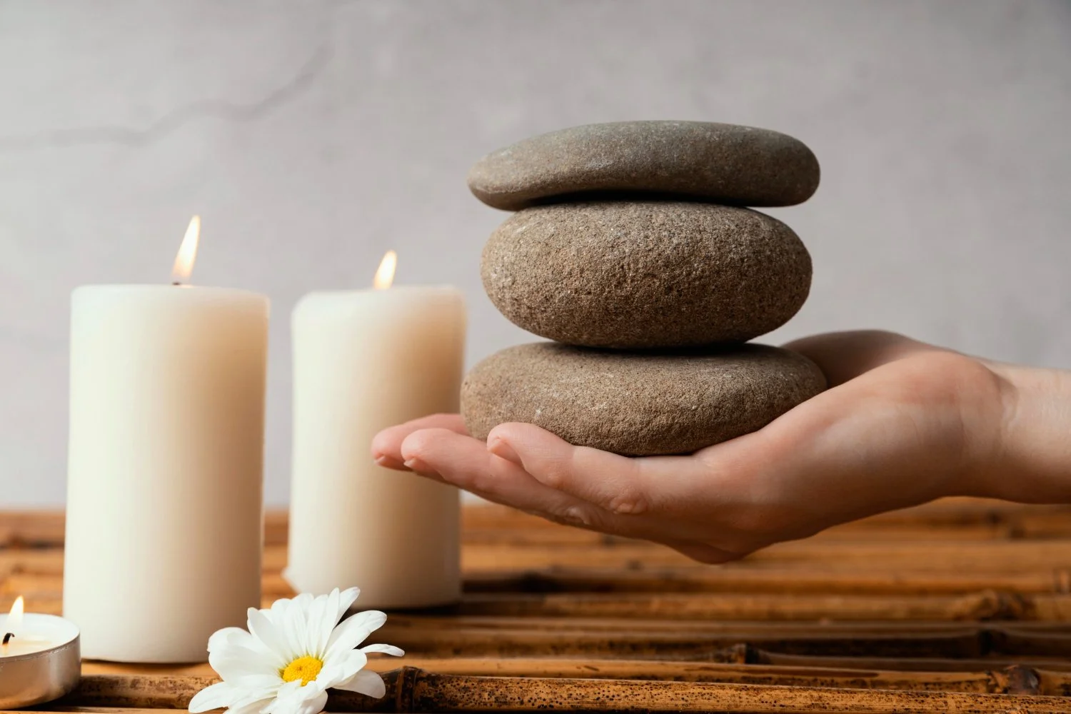 Hand holding stacked stones with candles in the background in a holistic practice space.