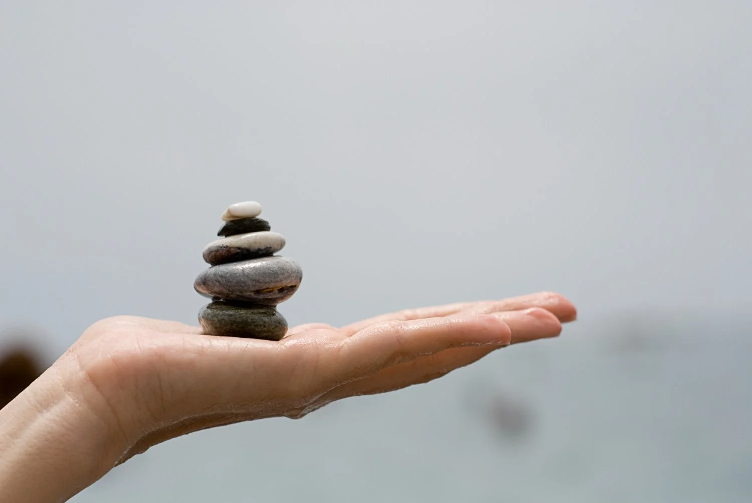 A hand balancing stones on as blurred greyed background.