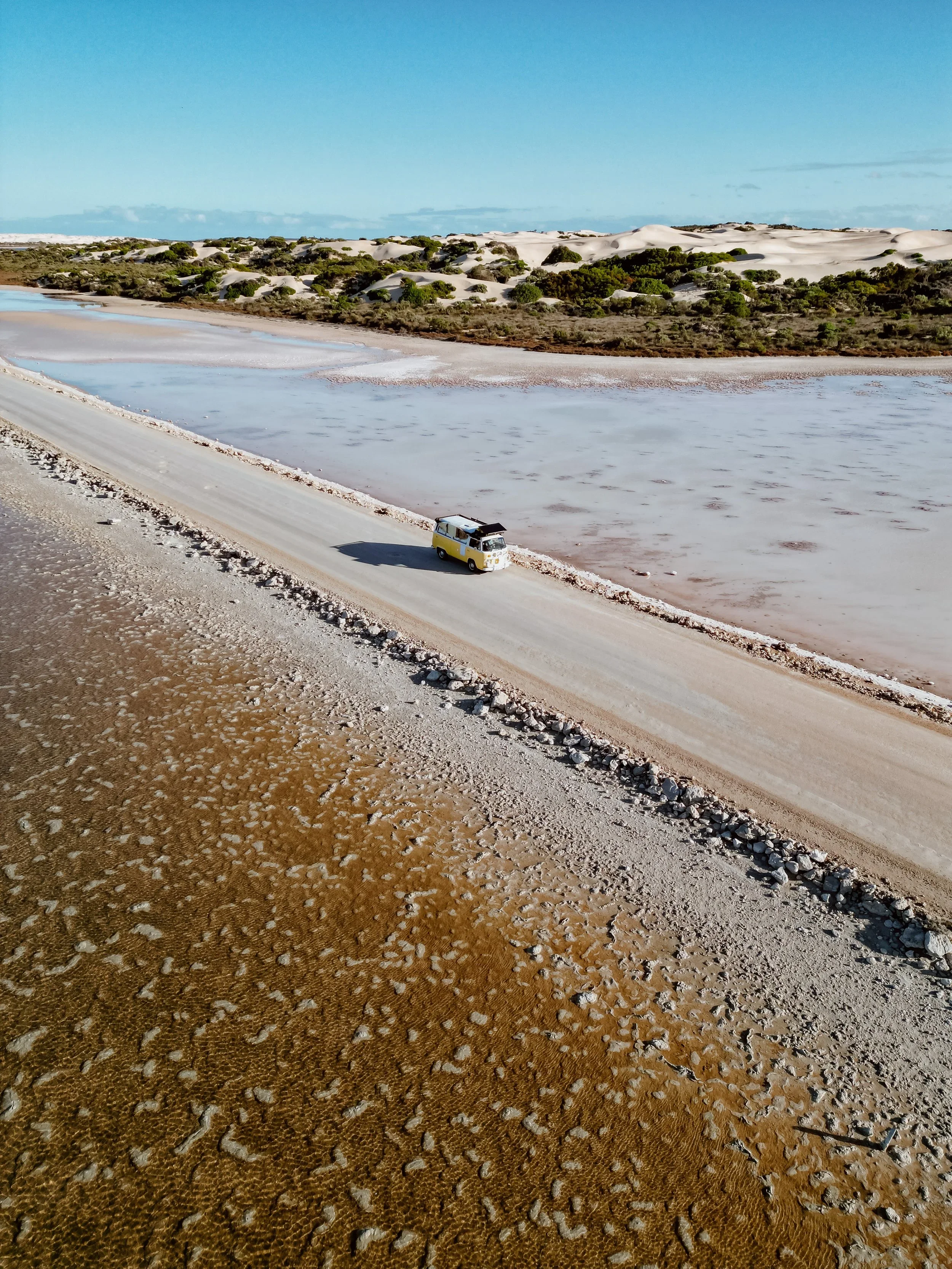 Yellow van driving through a road in the middle of the beach