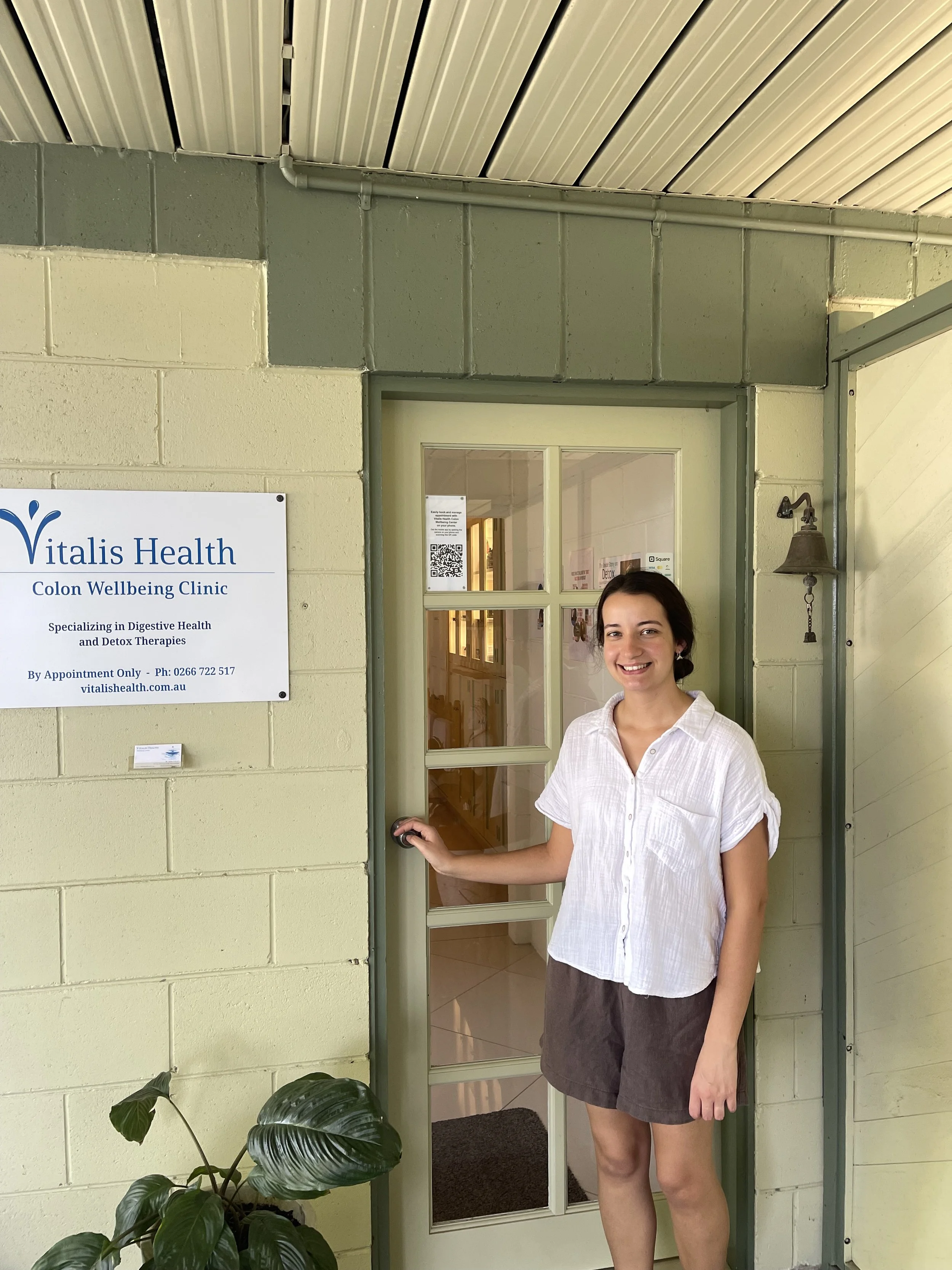 Justine, the practitioner in front of her home clinic with sage green painted doors.