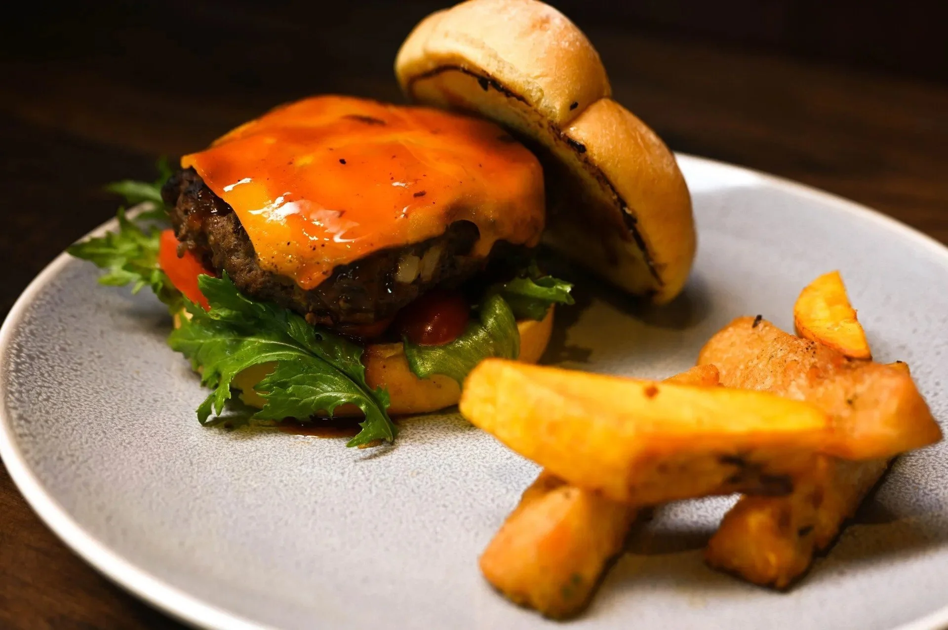 A cheeseburger with lettuce, tomato, melted cheese, and a beef patty, served on a white plate with French fries.