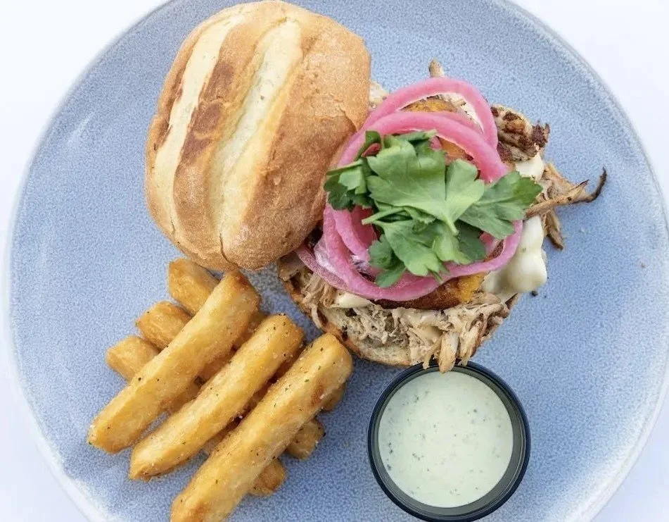 Pulled pork sandwich with pickled onions and cilantro, served with fries and a side of ranch sauce.