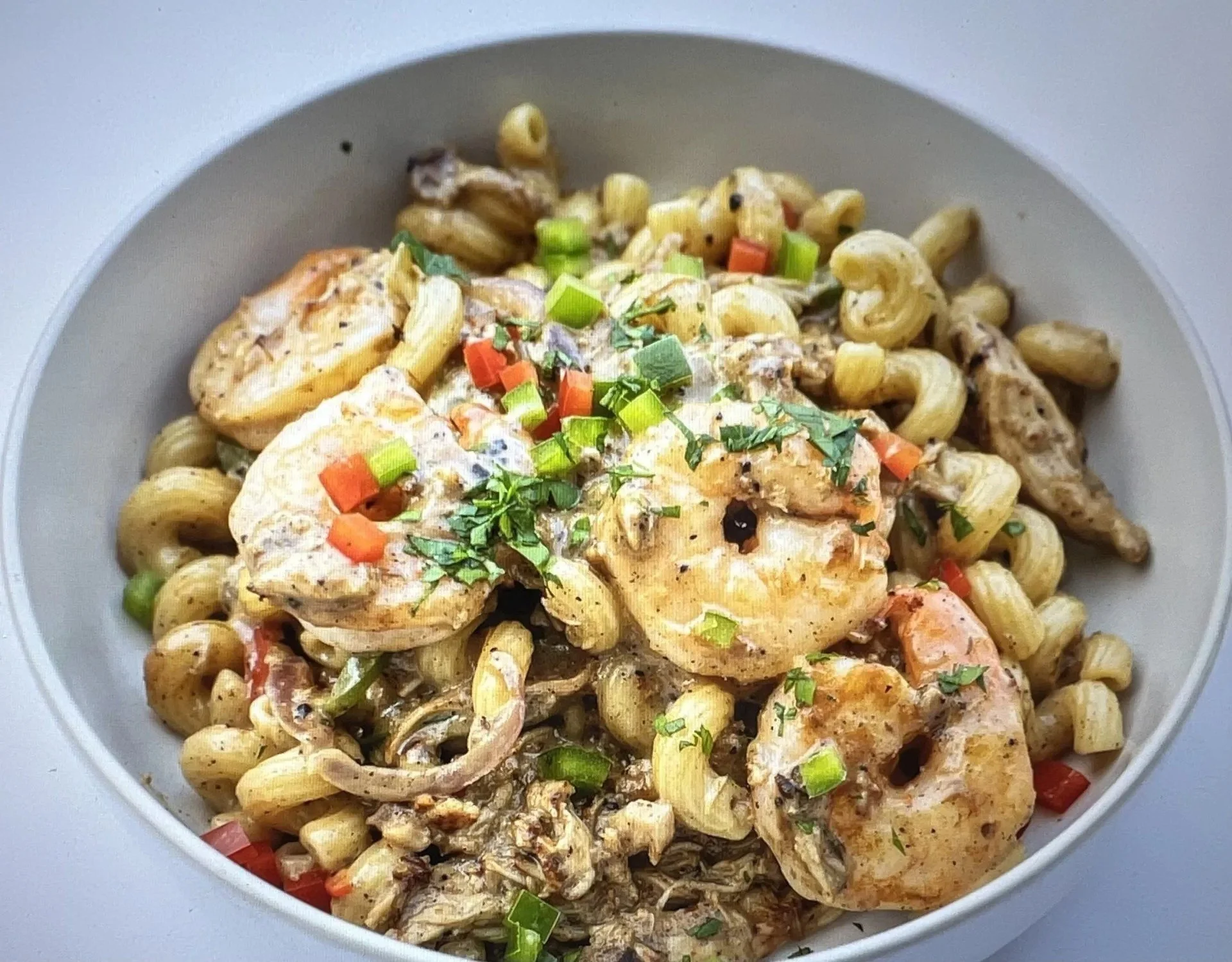 A bowl of cooked pasta topped with grilled chicken, chopped green and red peppers, herbs, and black pepper.