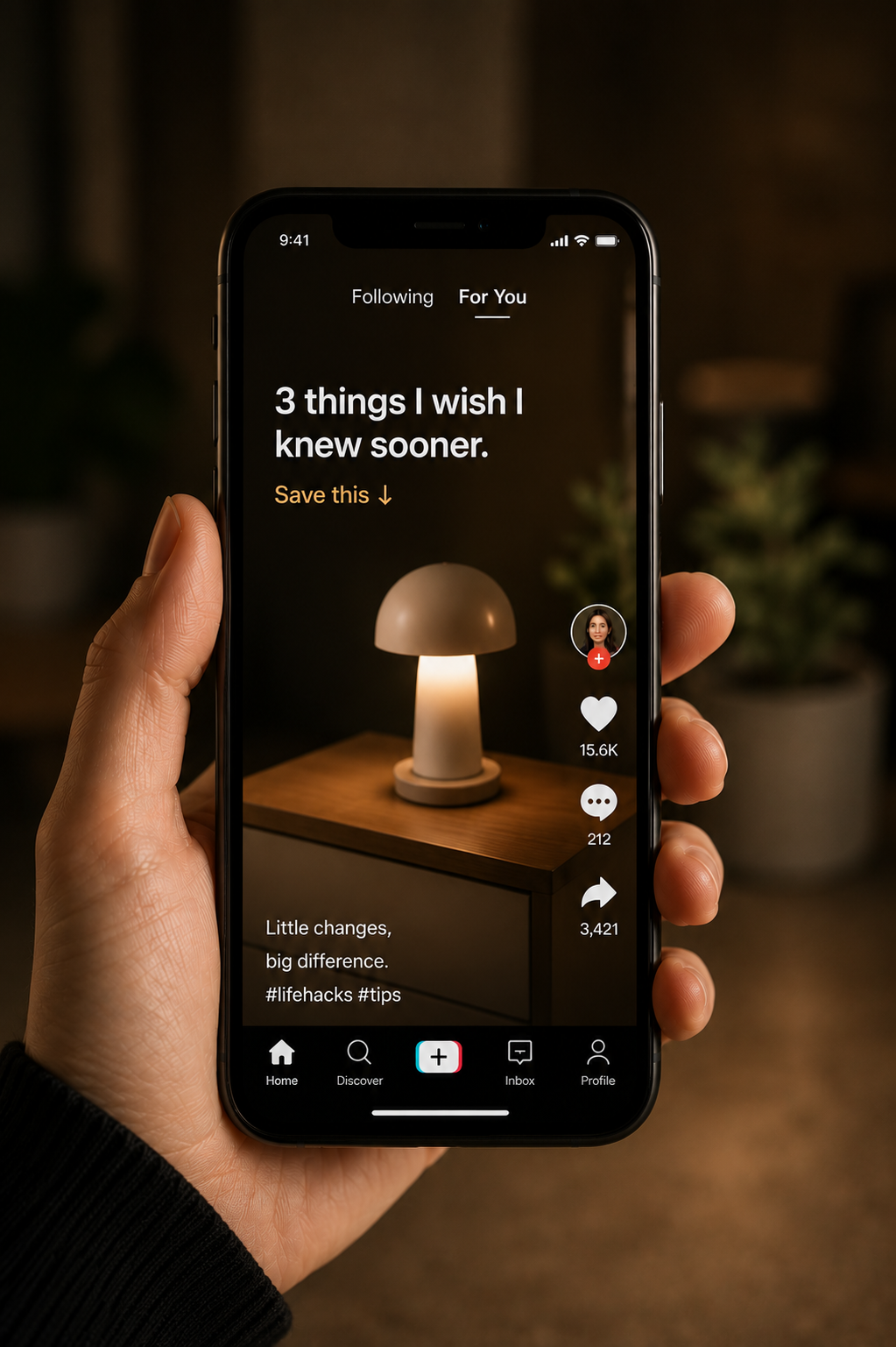 Close-up of a hand holding a smartphone displaying a TikTok video about three life hacks, with a dark background and a lamp on a wooden table in the video.