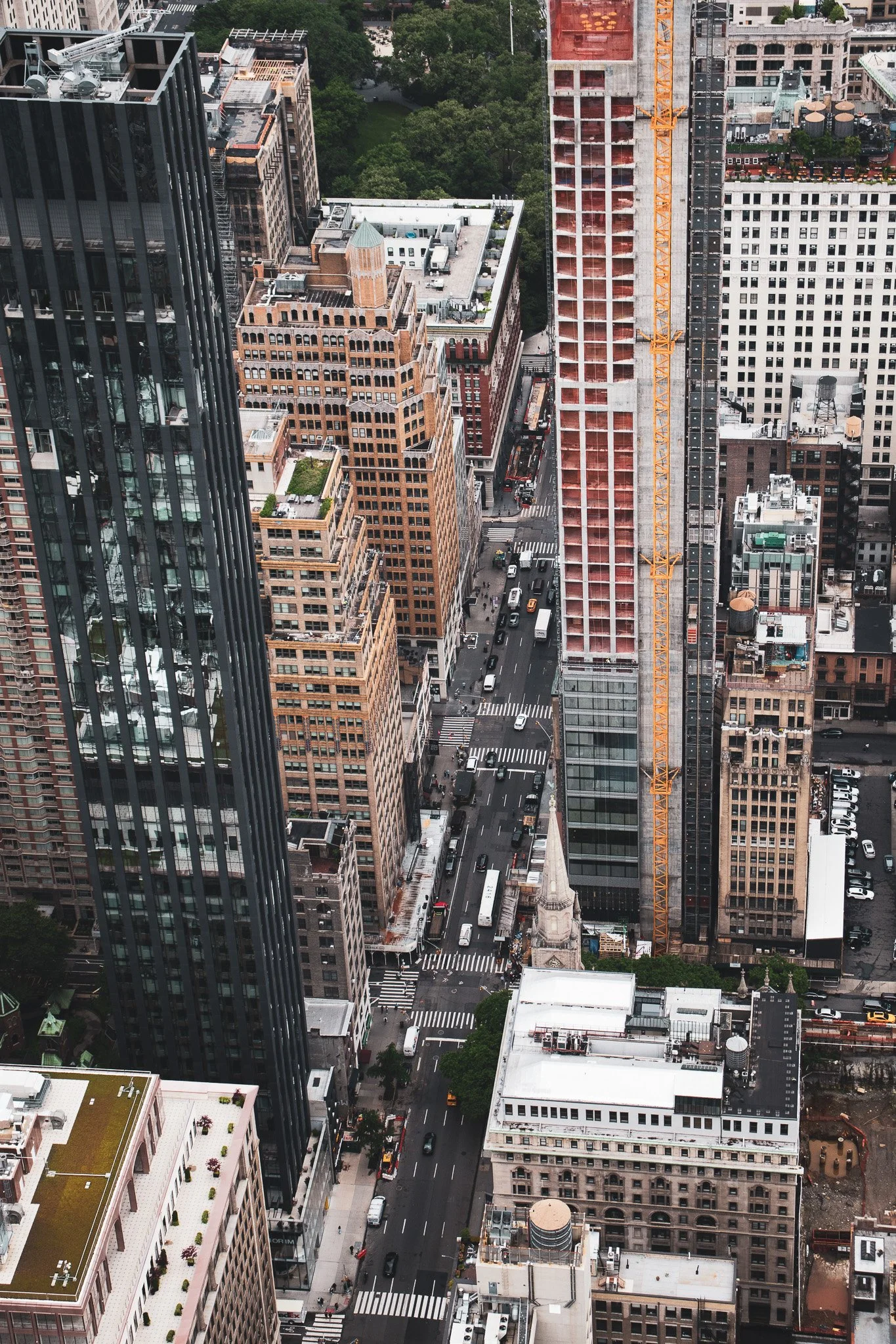 A high angle view of a city street with tall buildings, a construction crane, and cars on the road.