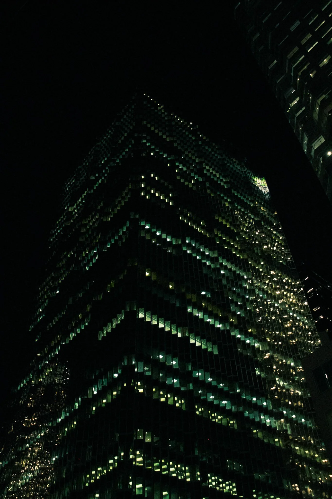 Nighttime cityscape showing tall high-rise buildings with illuminated windows and geometric patterns on their facades.