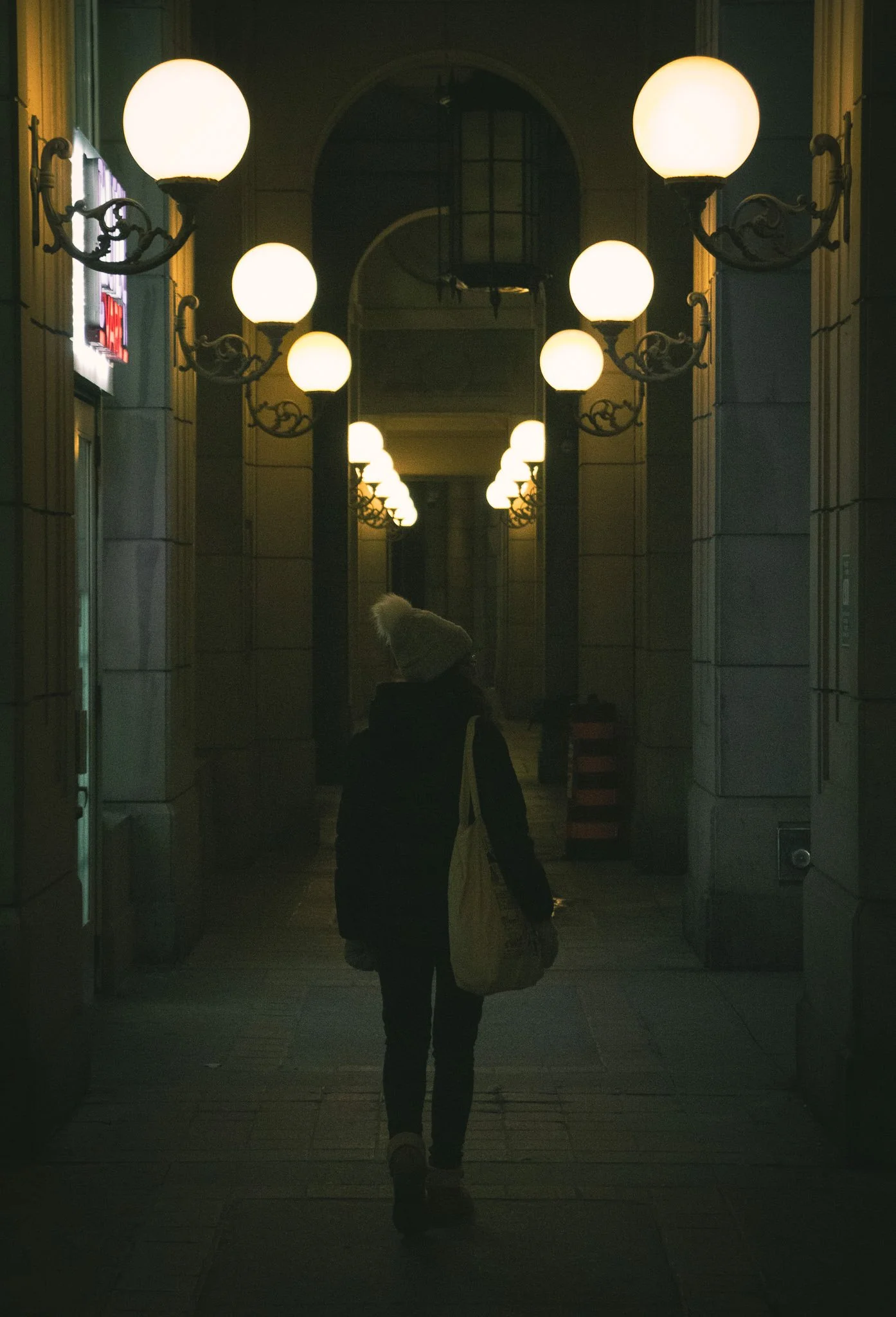 A person walking through a corridor with large glowing globe lights hanging from the ceiling.