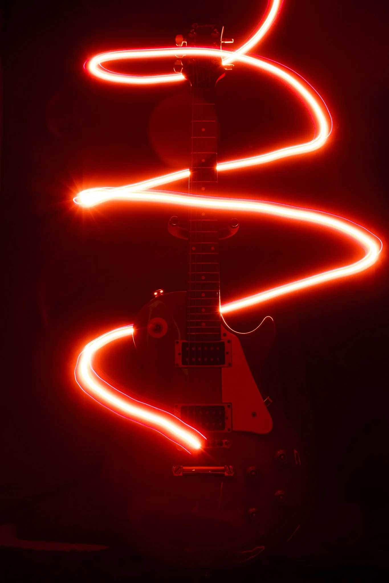 An electric guitar with red glow lights wrapped around it, creating a swirling pattern against a dark background.