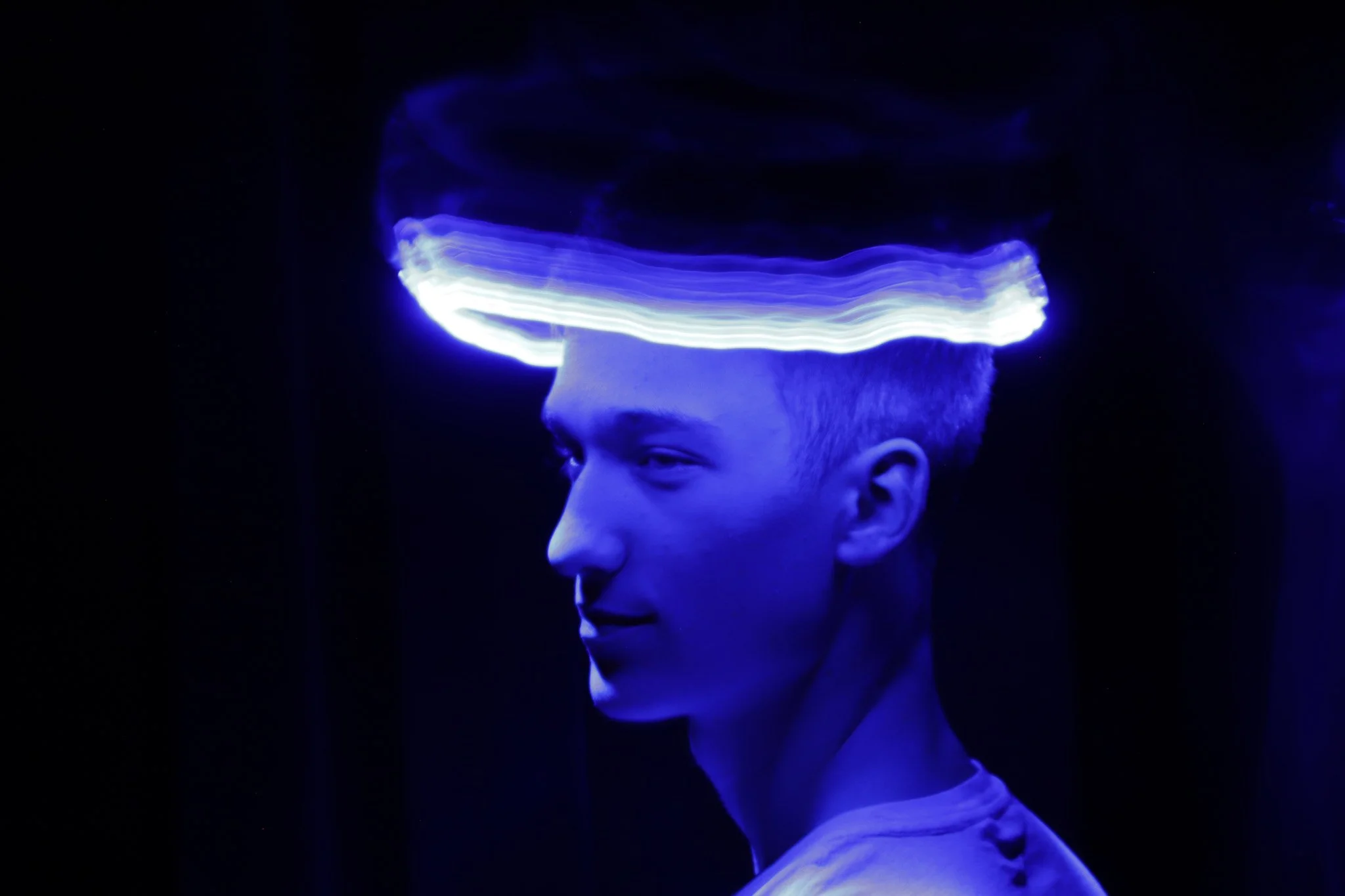 Profile of a young man with short blonde hair, illuminated by blue light, with a glowing ring around his head.