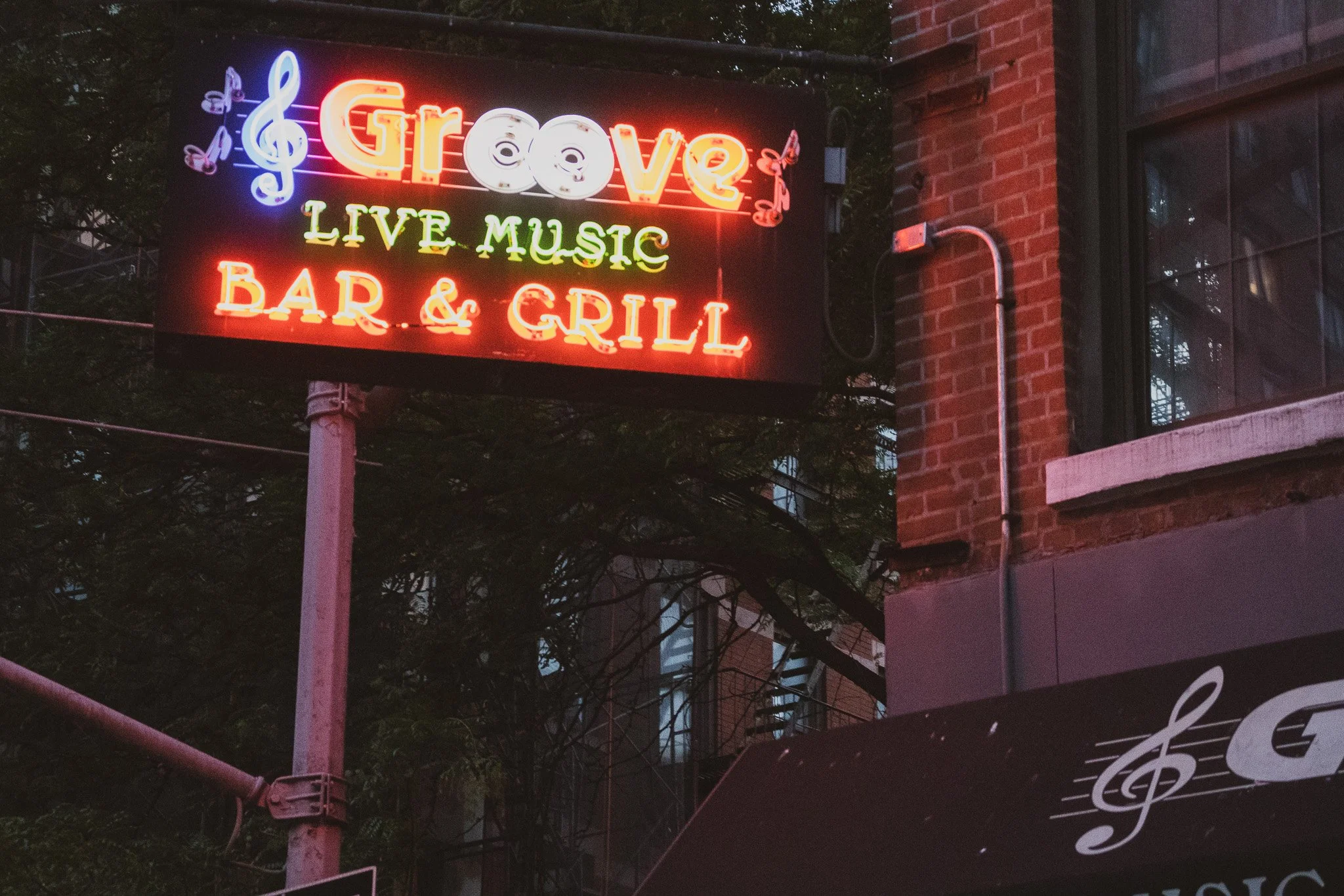 Neon sign advertising a live music venue called Greve, located in a brick building, with illuminated musical notes and text.