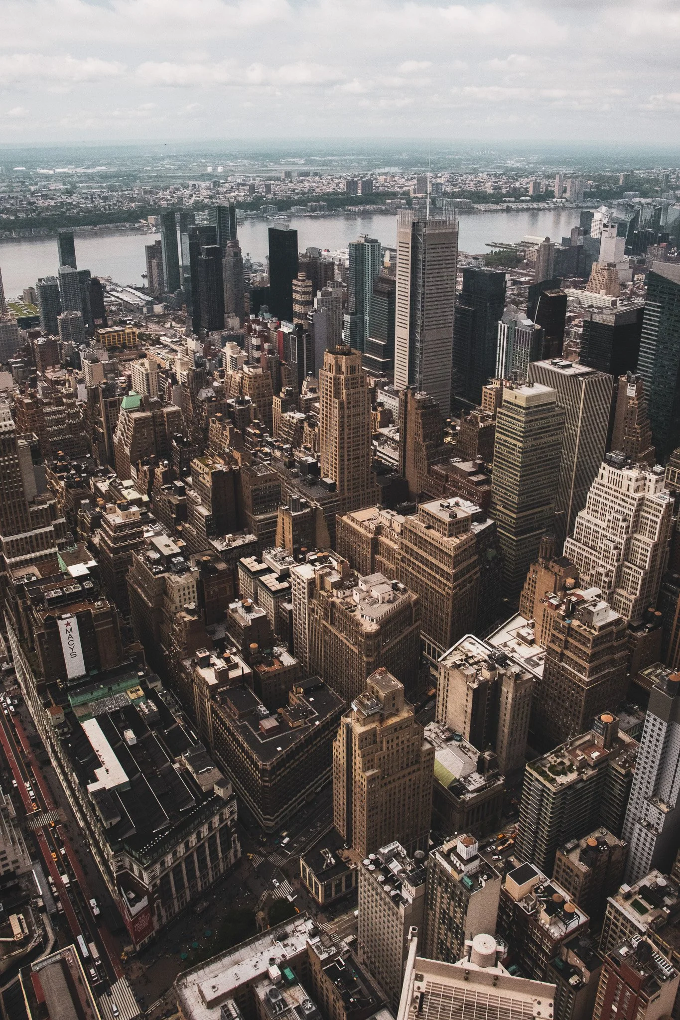 Aerial view of downtown Manhattan in New York City, showing numerous skyscrapers along the river, with clouds overhead.