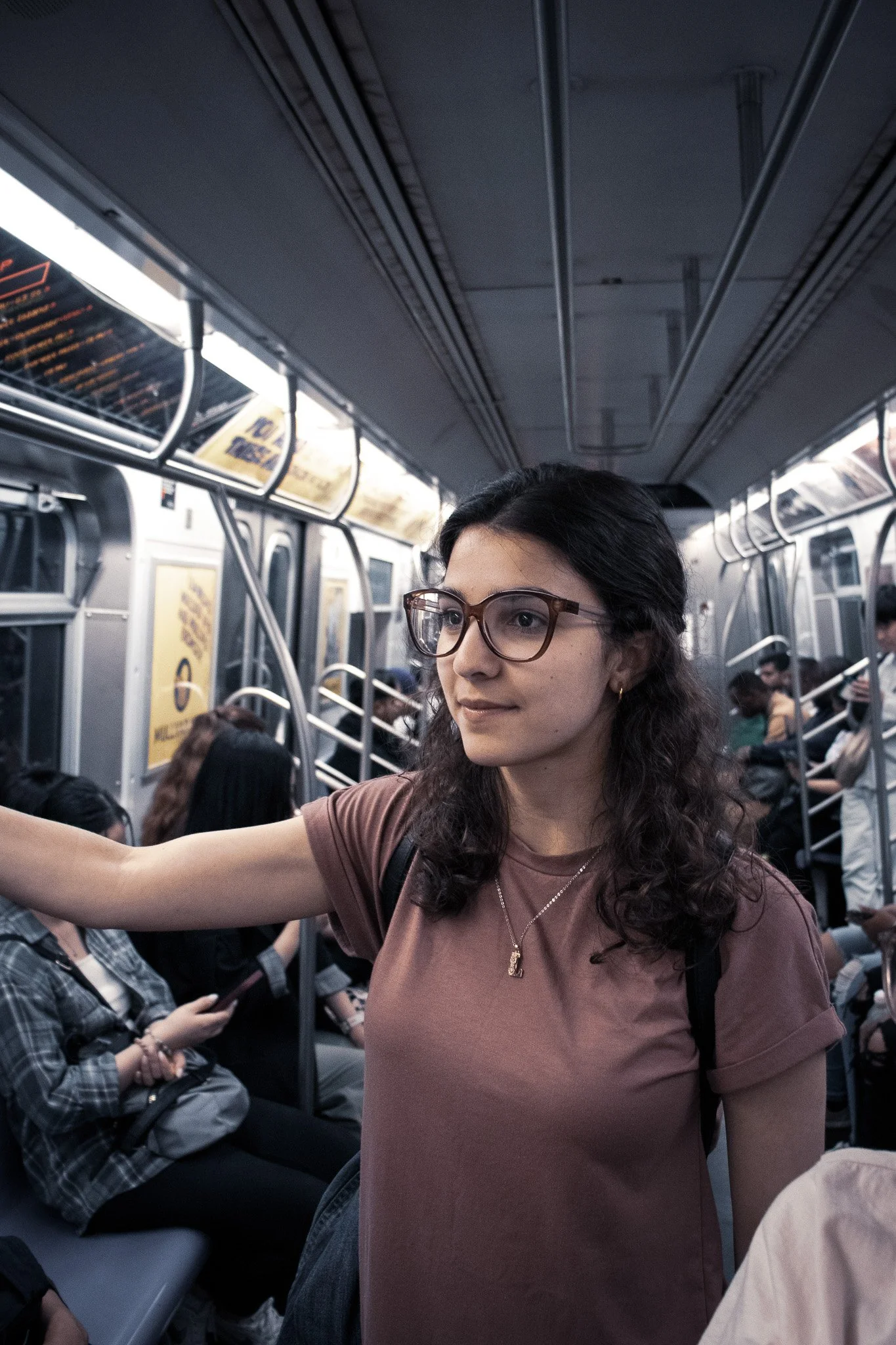 A woman with glasses and long curly hair taking a selfie on a crowded subway train.