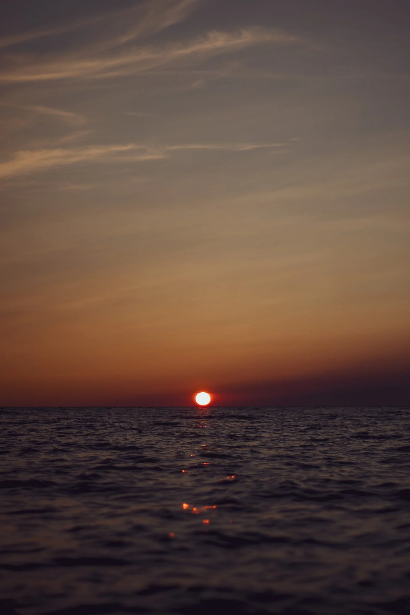 Sunset over the ocean with the sun near the horizon and clouds in the sky.