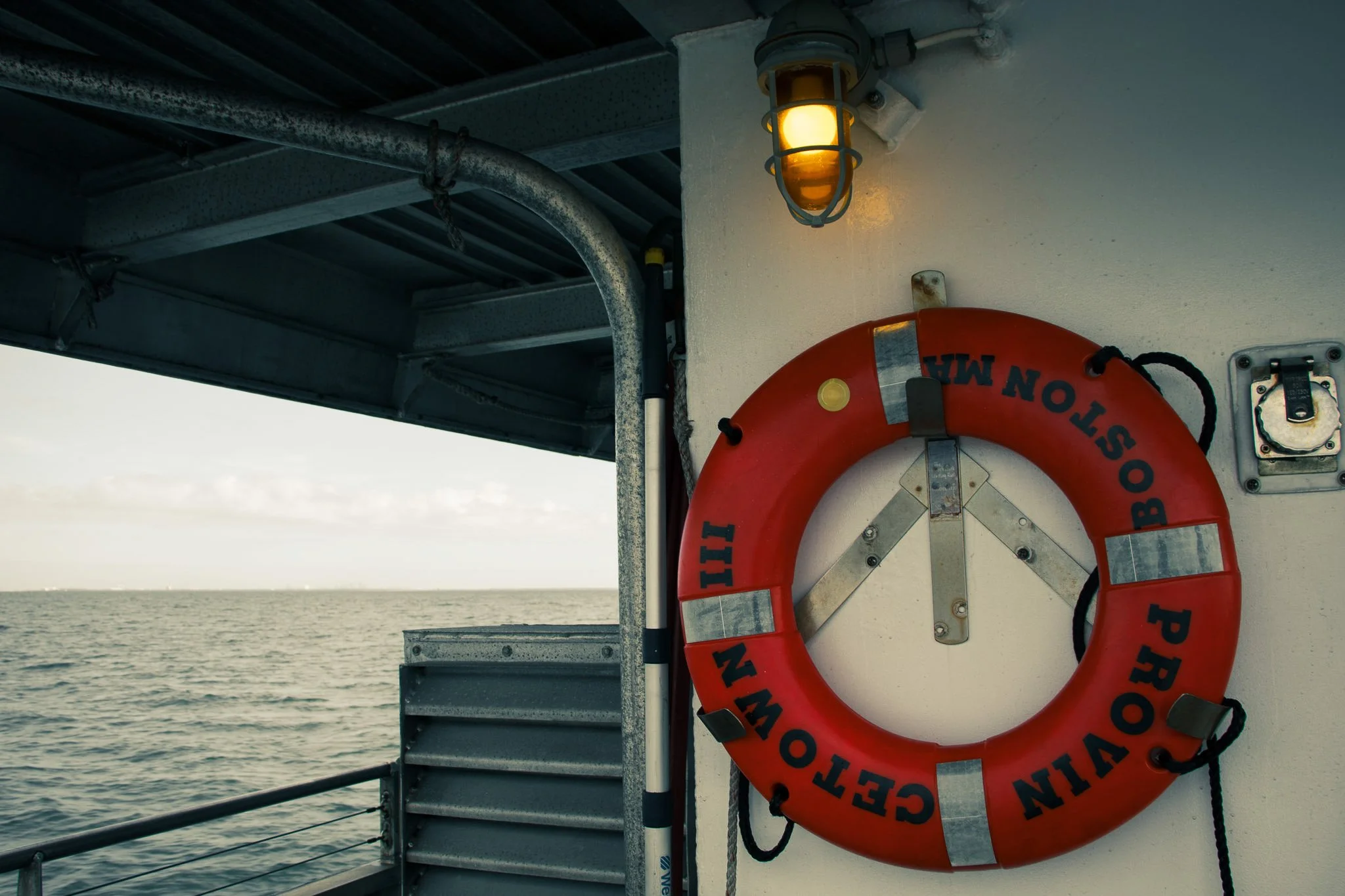 A life preserver hanging on the side of a boat near the water, with a yellow safety light above it, during daytime by the ocean.