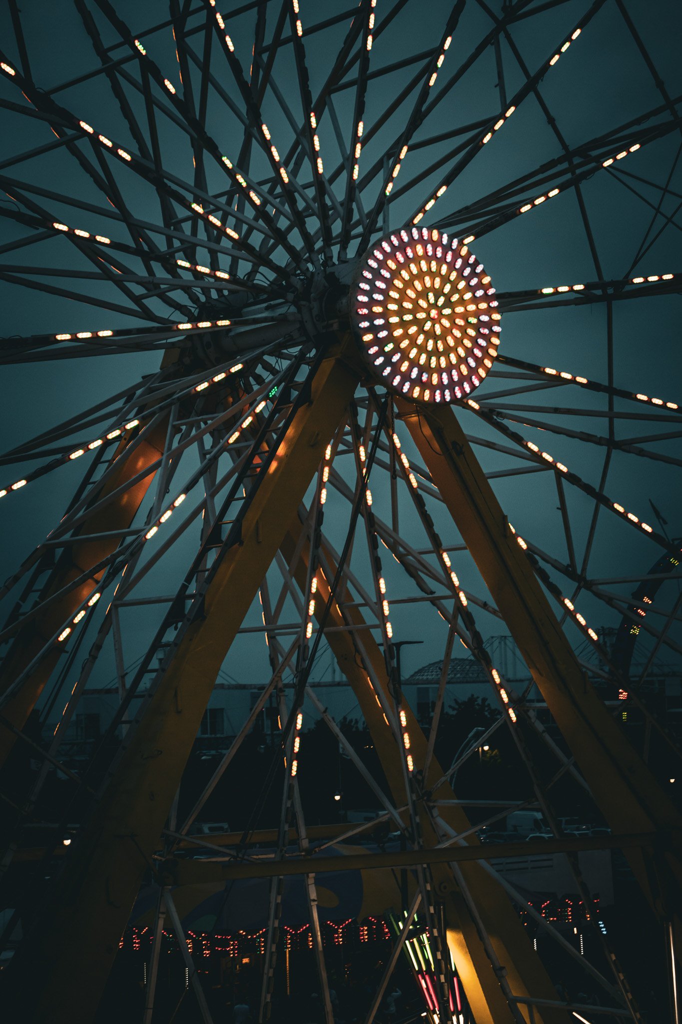 A Ferris wheel with bright lights at night, viewed from below, showing its circular structure and supporting beams against a dark sky.