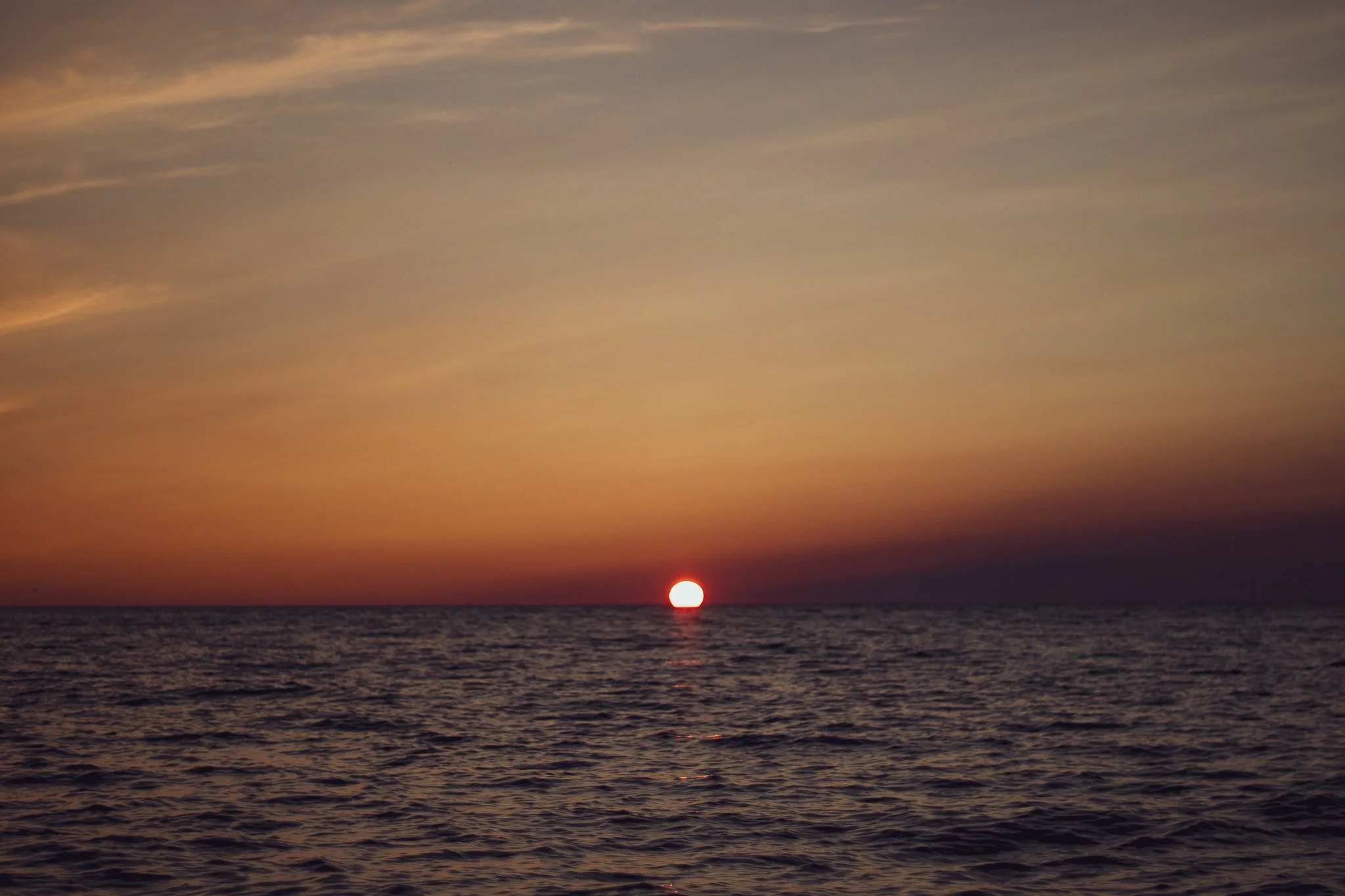 Sun setting over the ocean horizon with a sky filled with clouds, creating a peaceful and warm sunset scene.