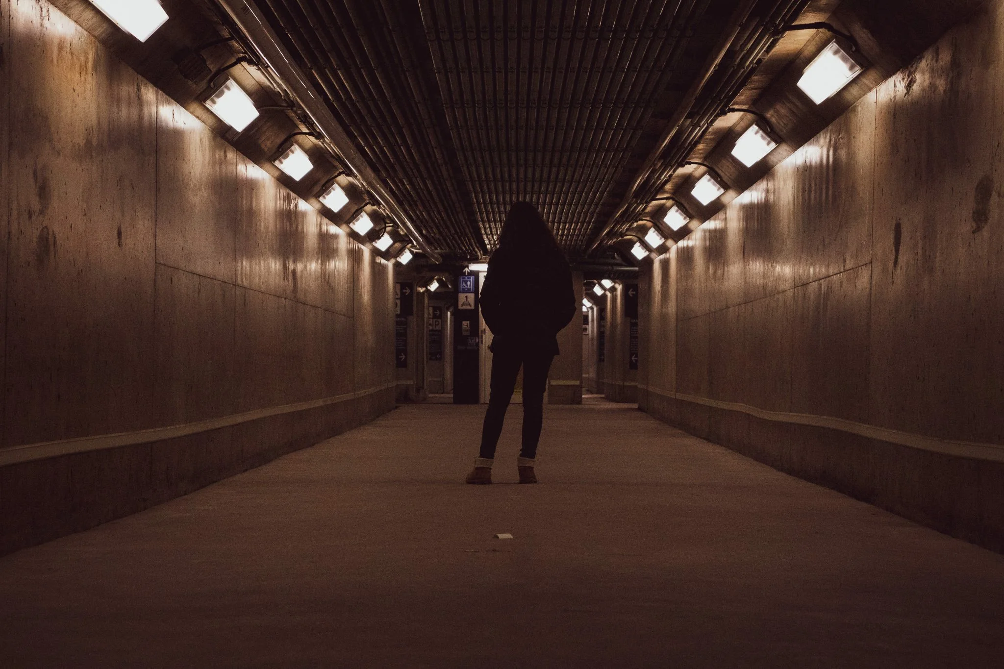 Person walking through an underground tunnel with illuminated lights on the ceiling.