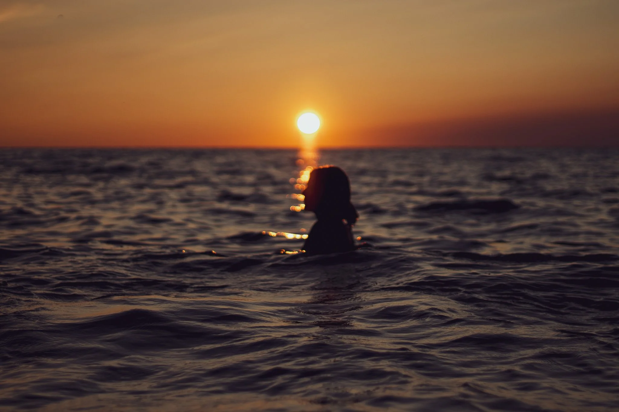 Person swimming in the ocean during a sunset with the sun low on the horizon.