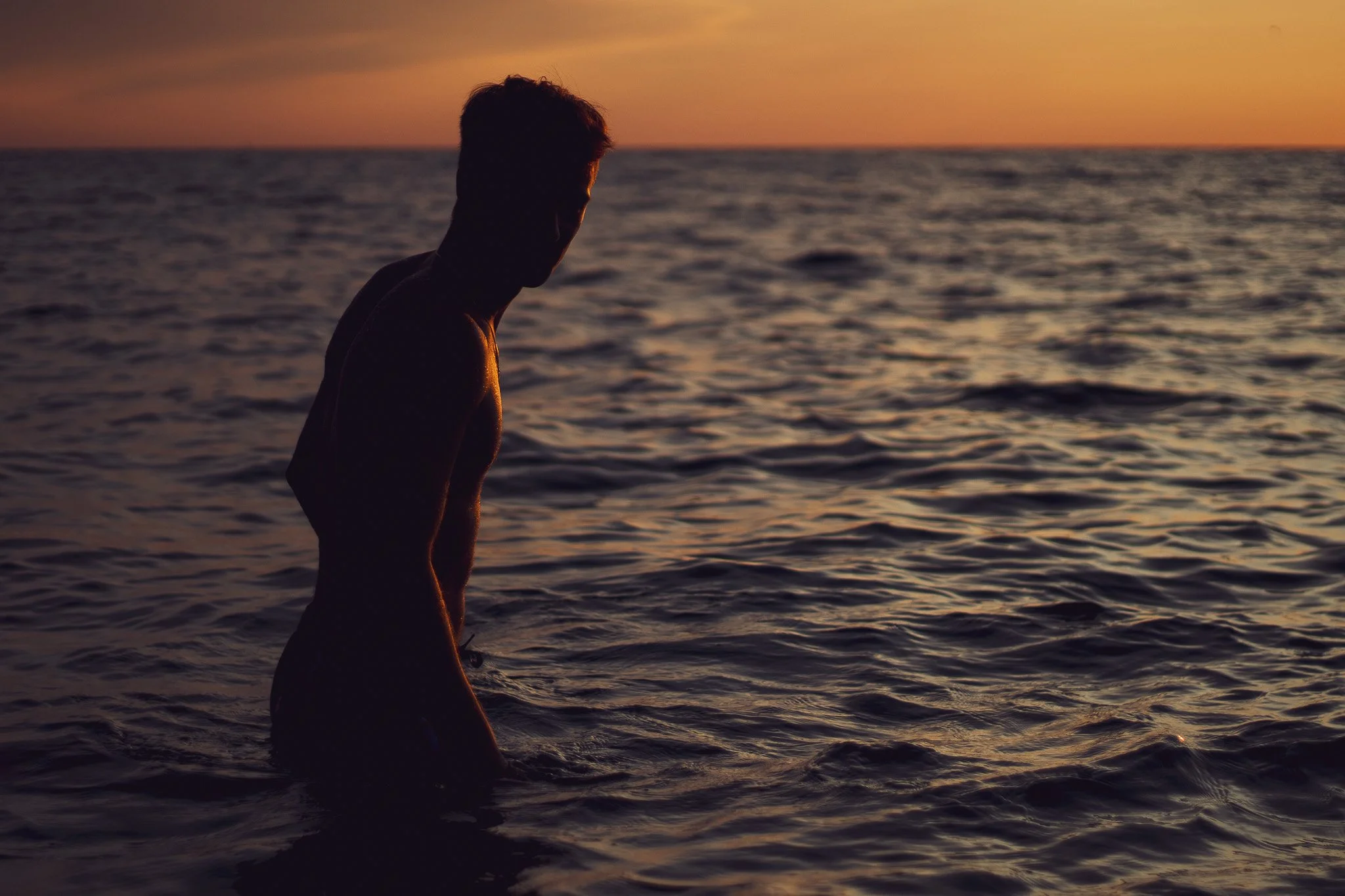 Silhouette of a person standing in the water, gazing at a sunset over the ocean.