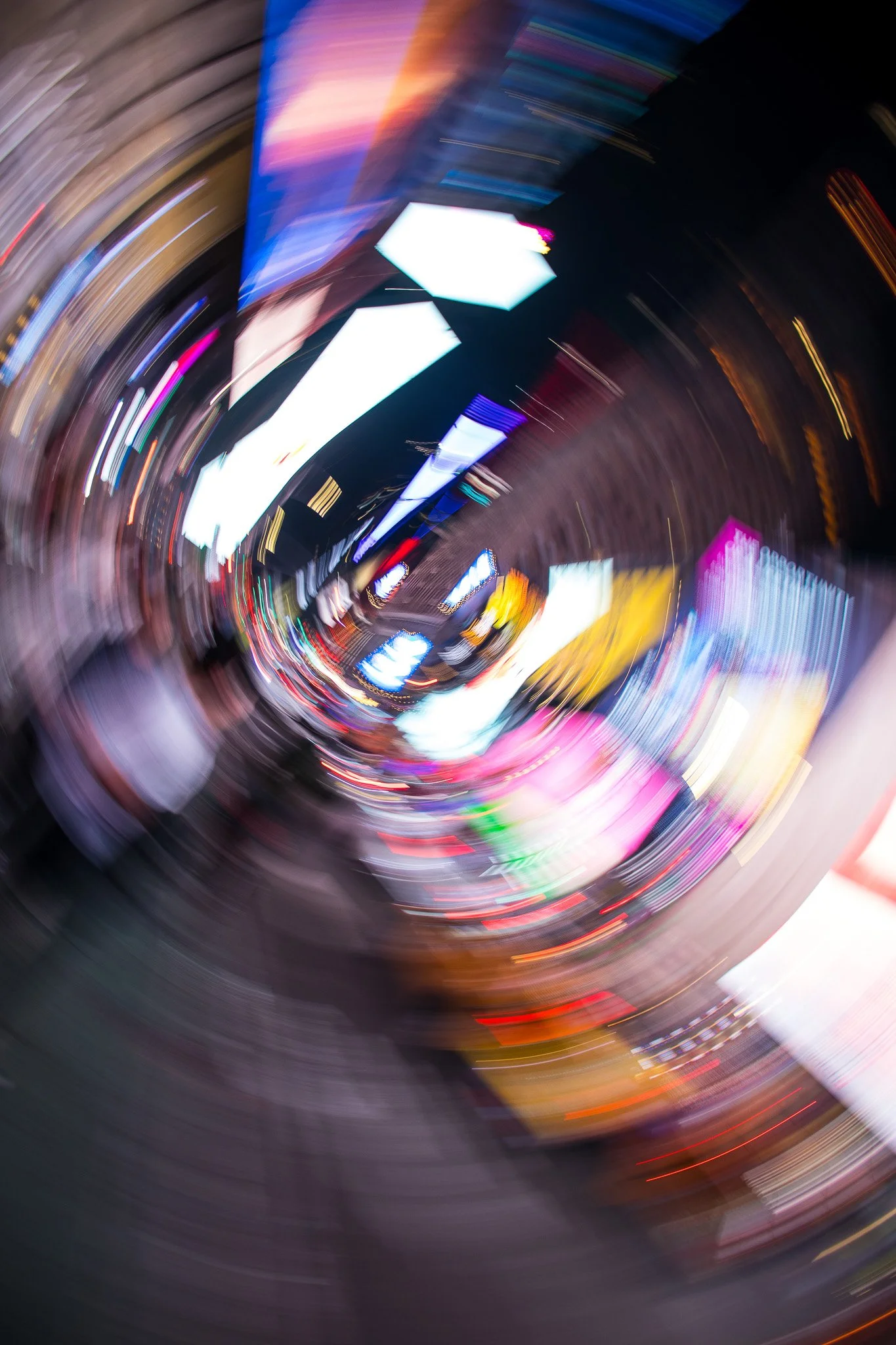 Blurred city lights and digital billboards at night, captured with a motion blur effect, creating swirling patterns of colorful lights.