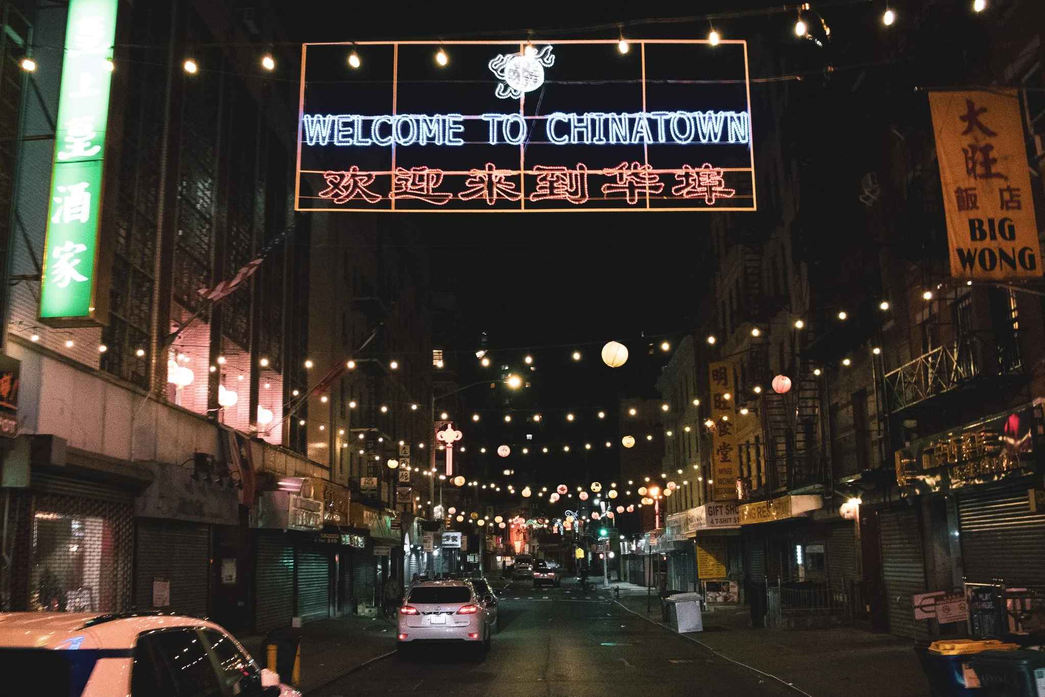 Night scene of Chinatown street with neon signs and string lights, including a prominent sign that says 'Welcome to Chinatown' and Chinese characters.