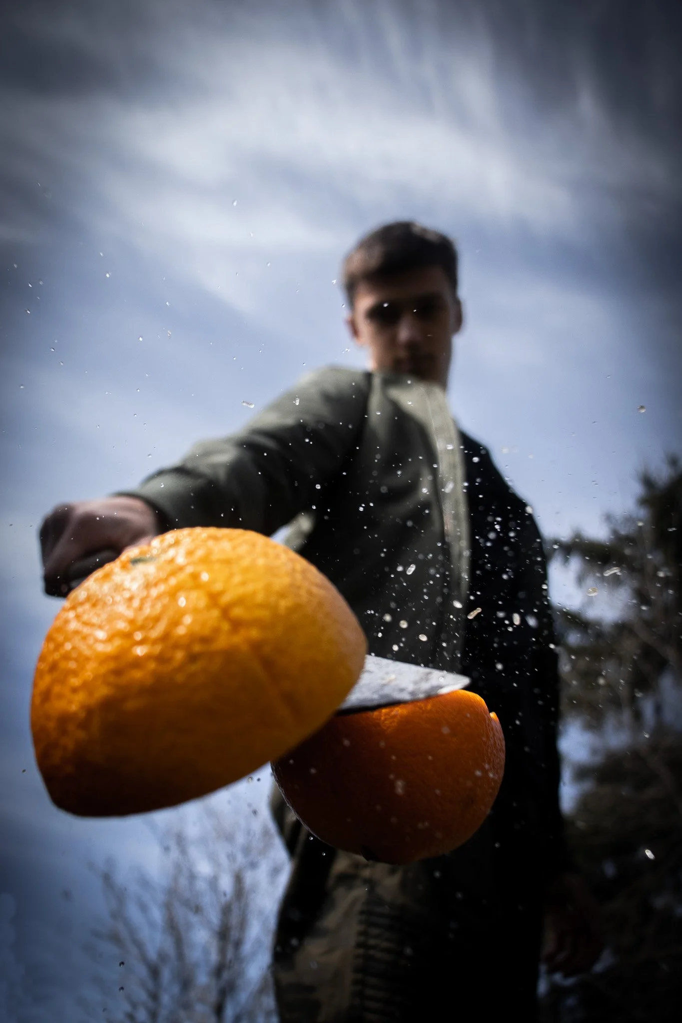 Person holding an orange in the foreground with snow and trees in the background.