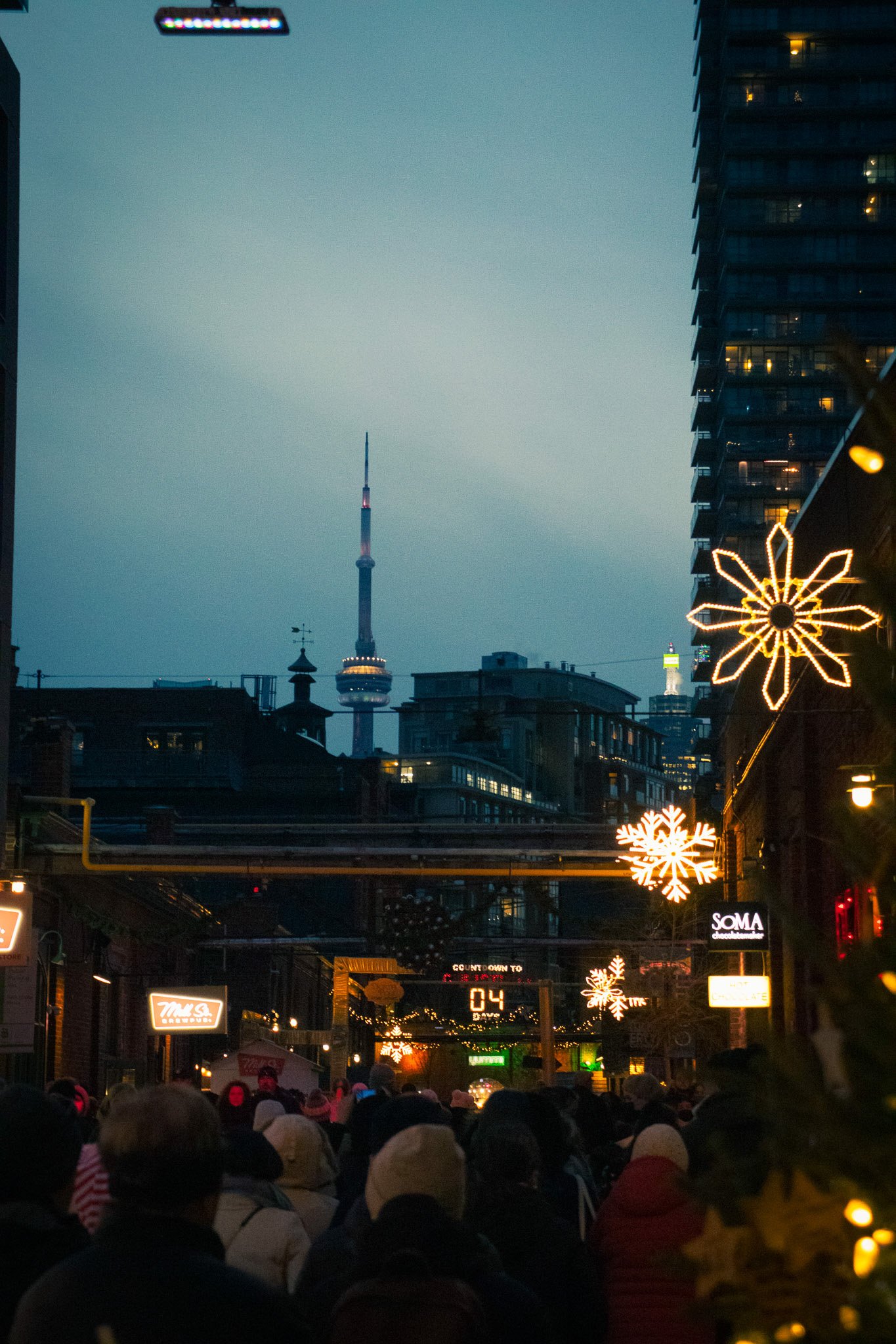 A city street scene at dusk with a crowd of people, holiday lights, and the Tokyo Skytree tower in the background.