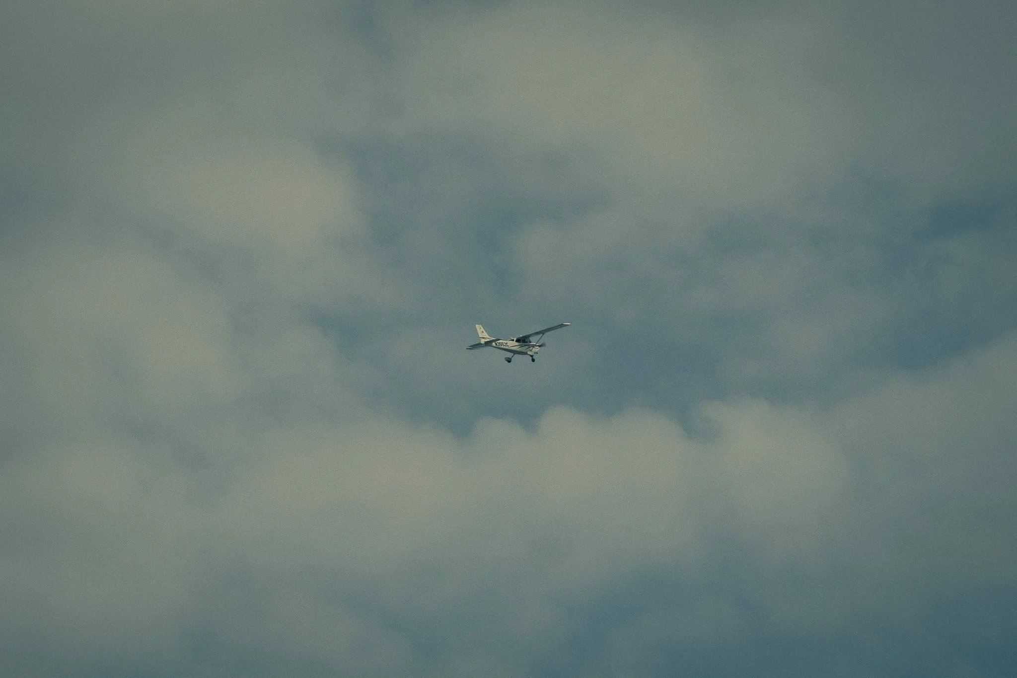 Small white airplane flying through cloudy sky.