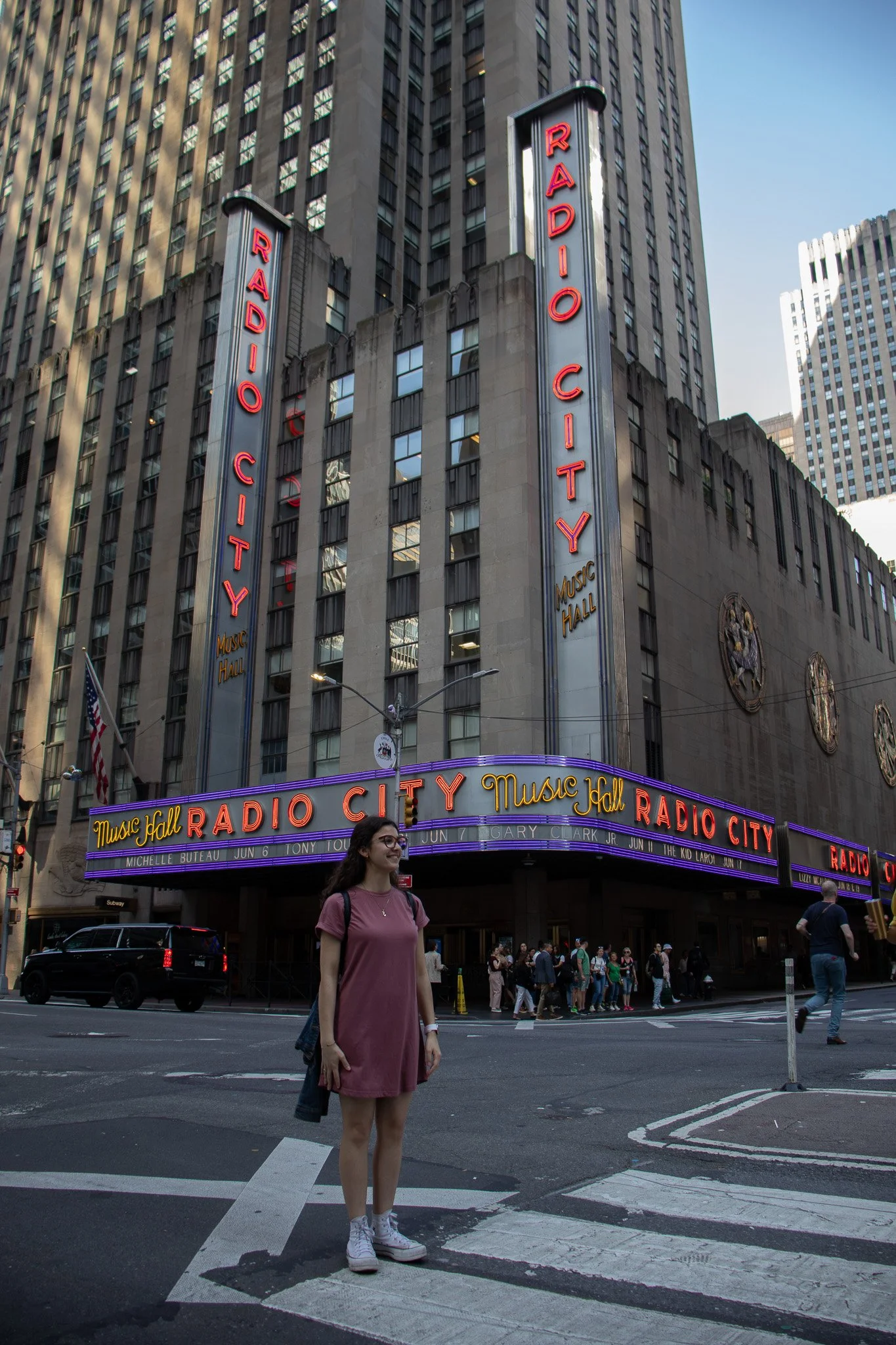 Woman standing at the crosswalk in front of Radio City Music Hall with a crowd and cars in New York City