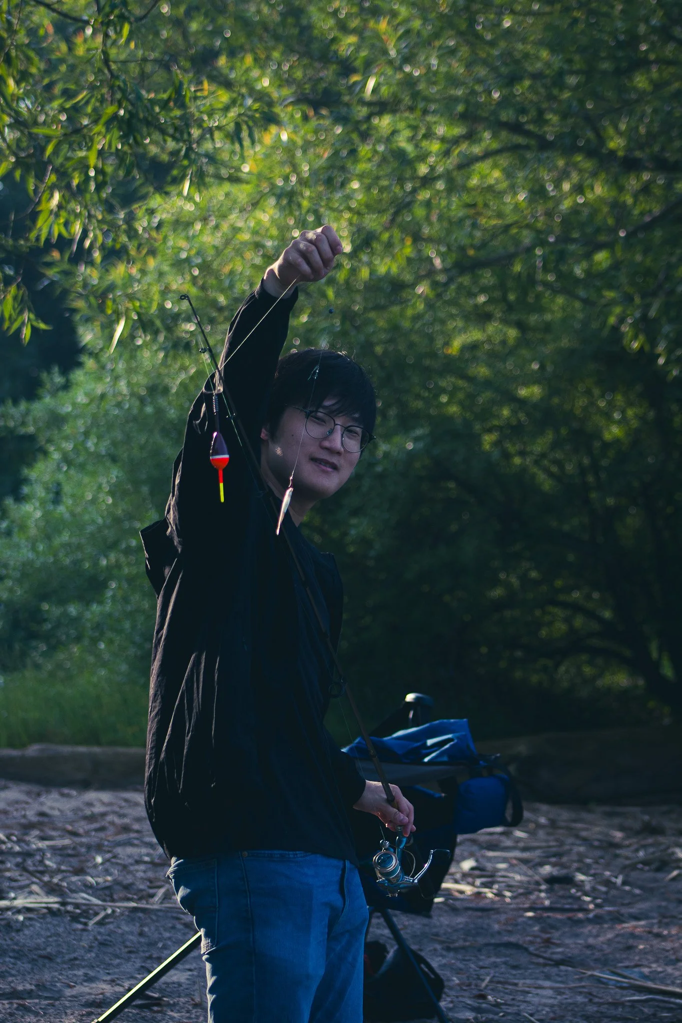 Person holding a fishing rod with a float attached, standing outdoors in a wooded area.