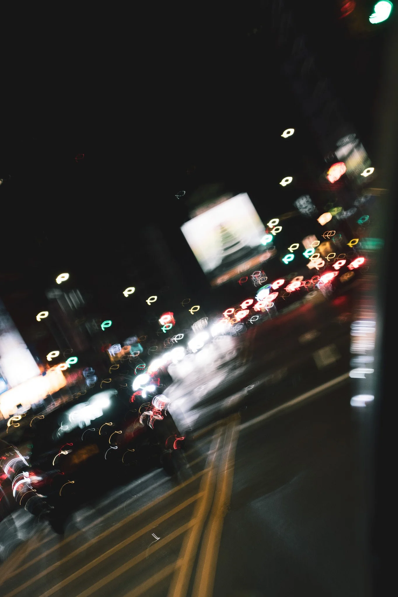 Nighttime street scene with blurred colorful car lights, traffic signals, and illuminated signs, creating a dynamic, abstract view of city traffic.