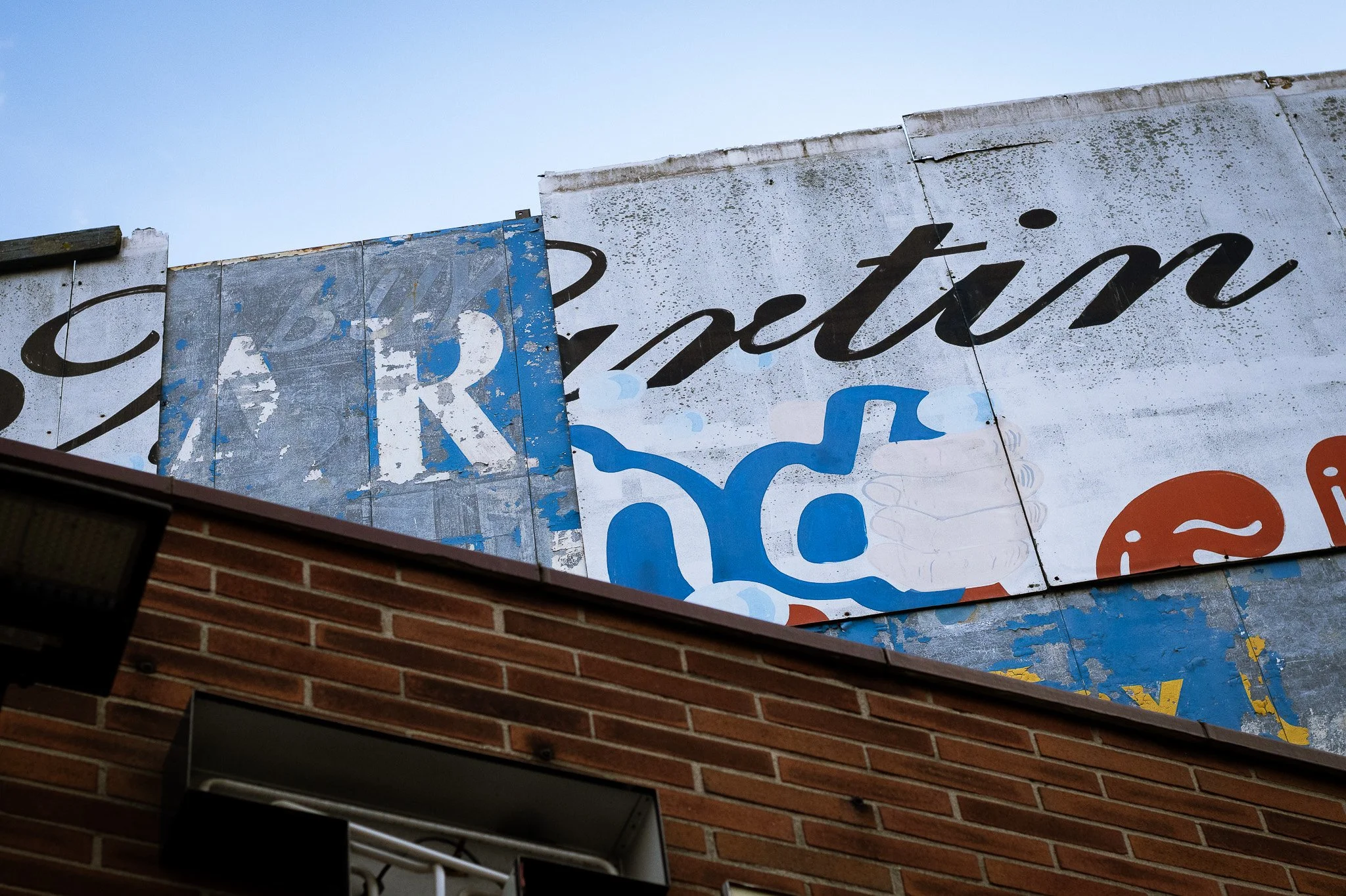 Close-up of a weathered sign with part of the word 'Restaurante' visible, mounted on a brick wall, under a clear blue sky.
