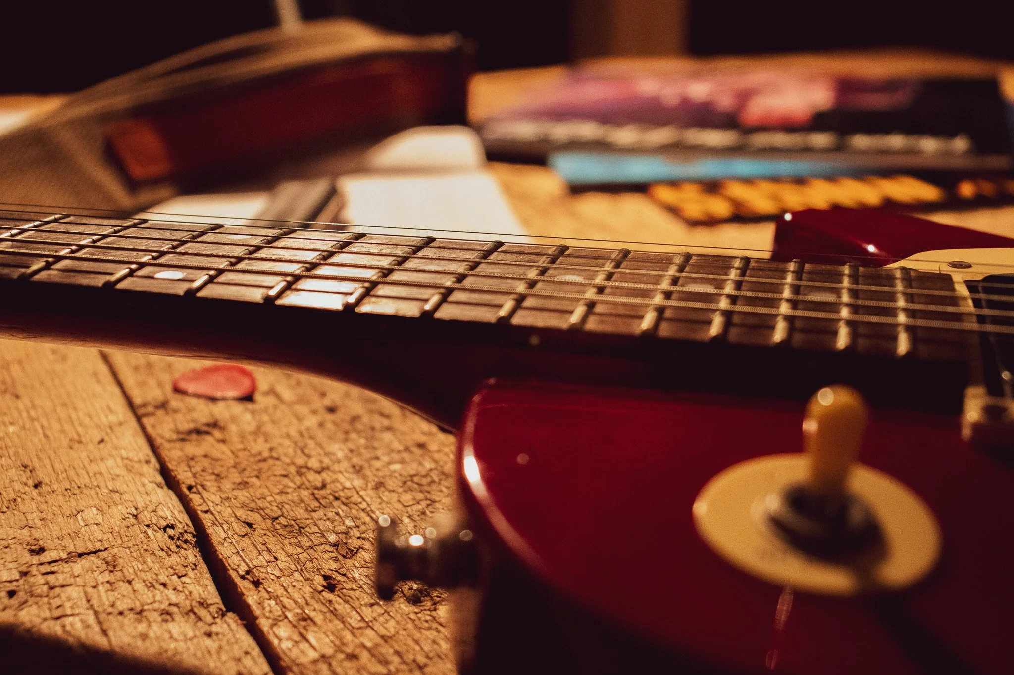 An electric guitar resting on a wooden surface with various colorful objects in the background, slightly out of focus.