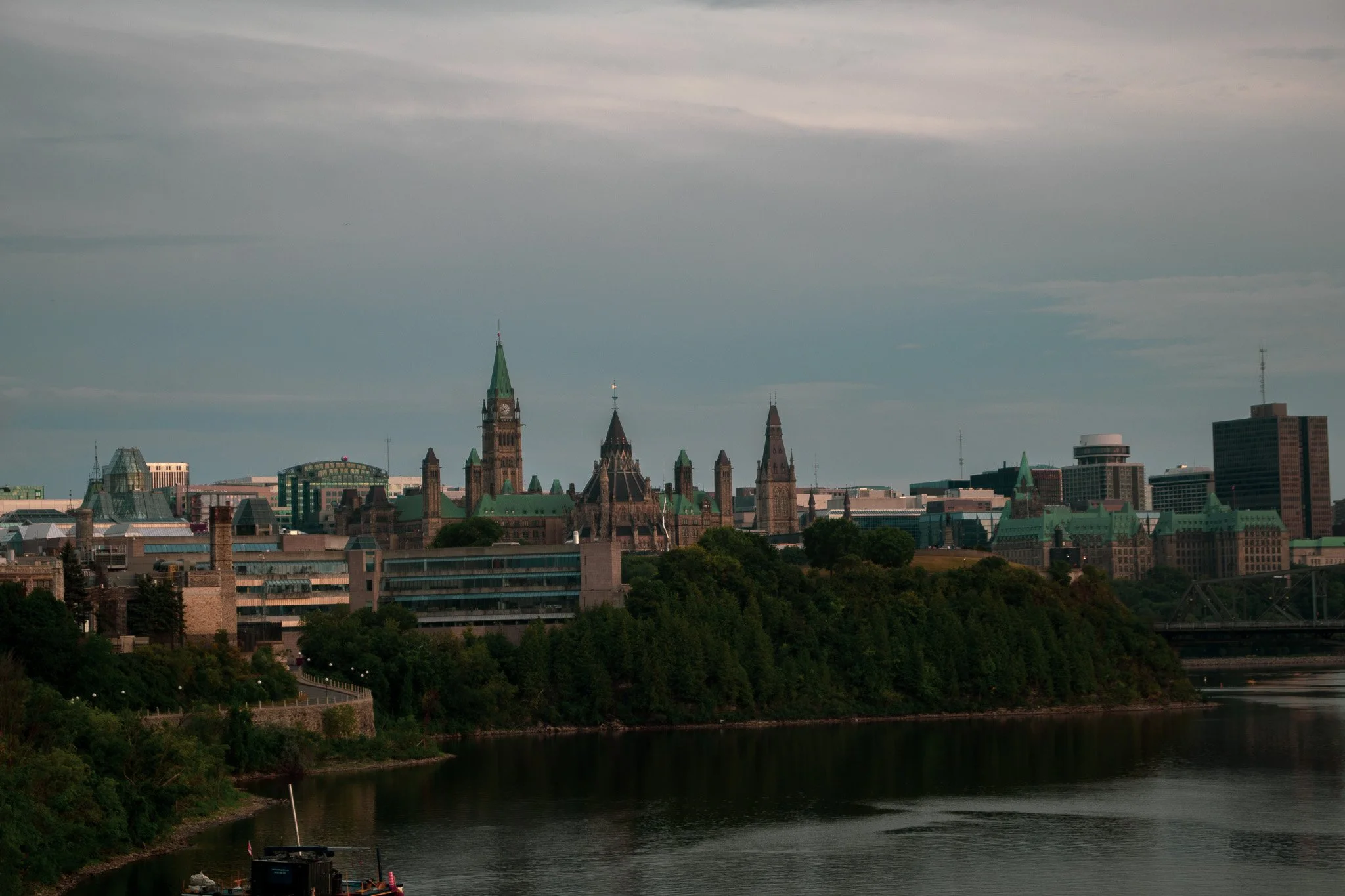 City skyline featuring historical and modern buildings with a river in the foreground and an overcast sky.