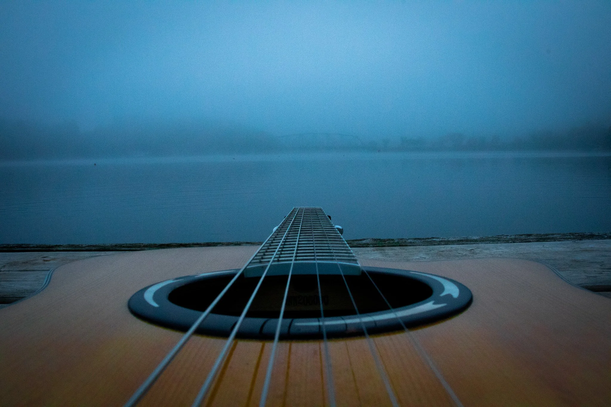Close-up view from the body of an acoustic guitar pointing towards the sky, with the sky and some clouds in the background.