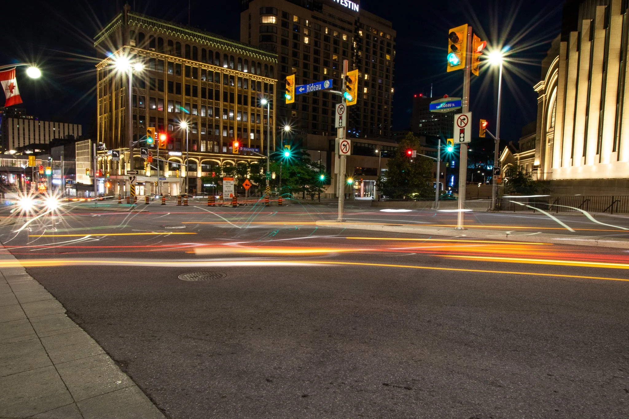Nighttime city street scene with traffic lights, illuminated buildings, and light streaks from moving vehicles.