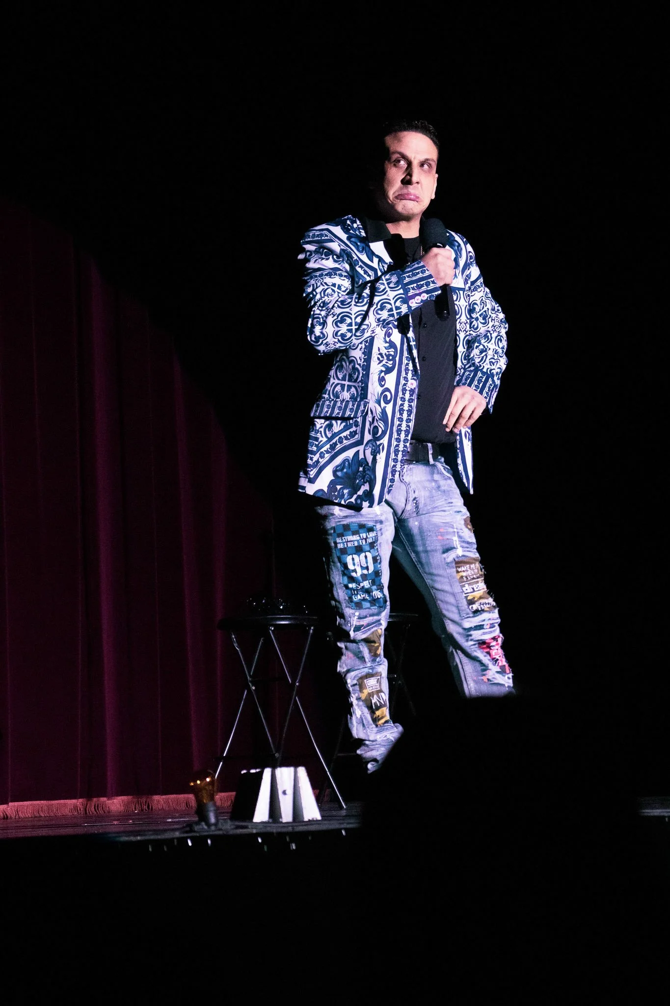 Man performing on stage holding a microphone with a dark background.