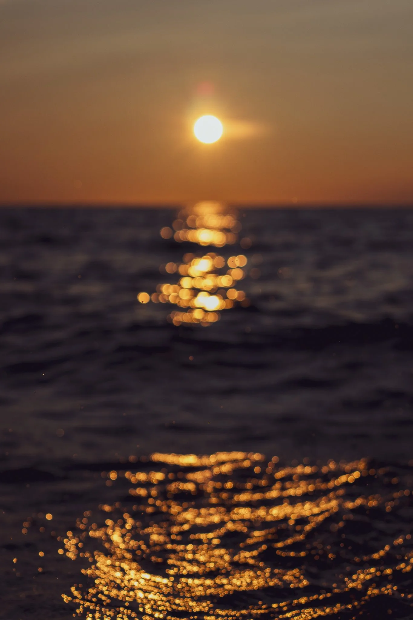 A sunset over the ocean with the sun's reflection shimmering on the water.