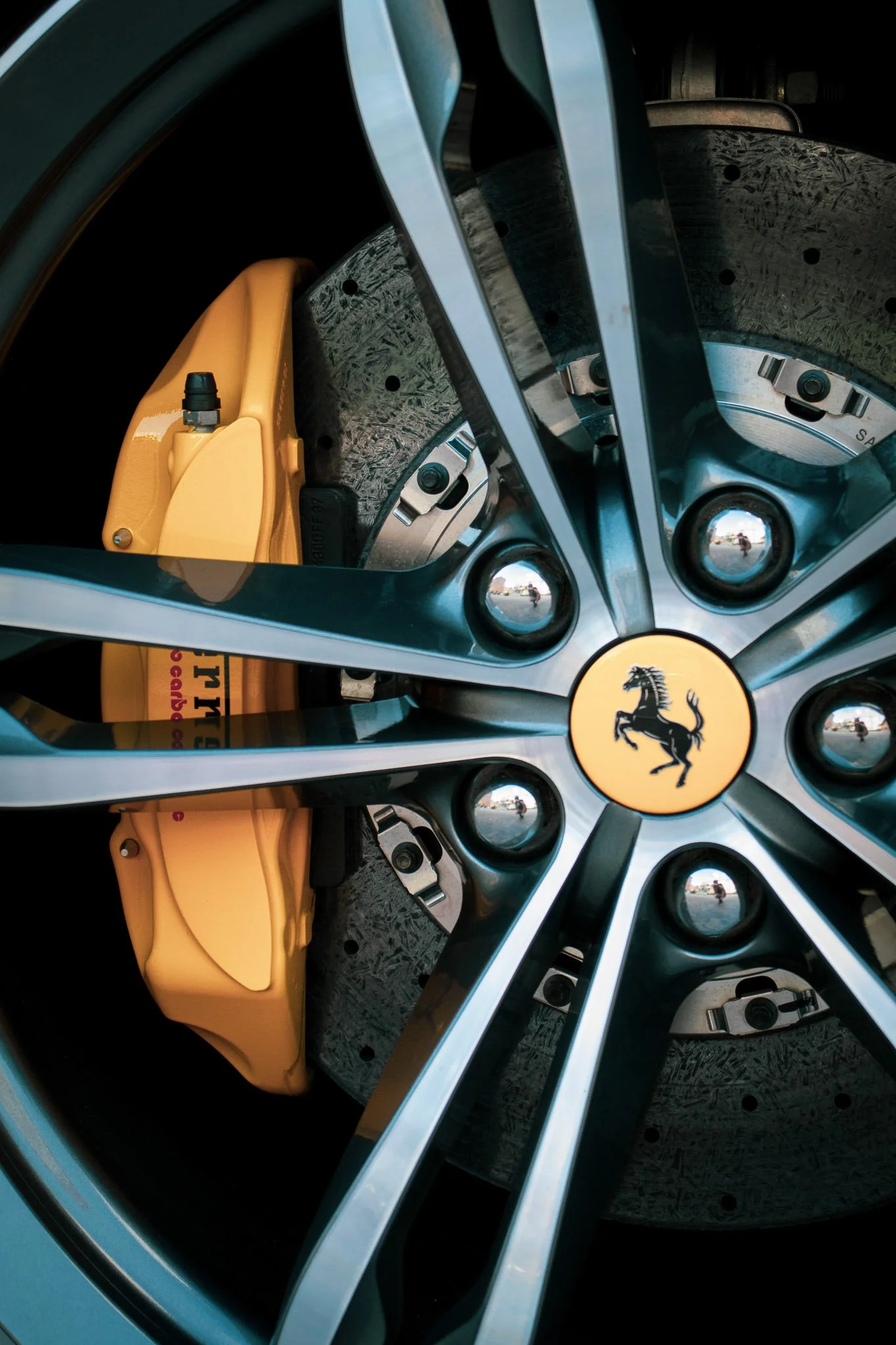 Close-up of a Ferrari car wheel showing a brake caliper, brake disc, and the Ferrari logo on the hubcap.