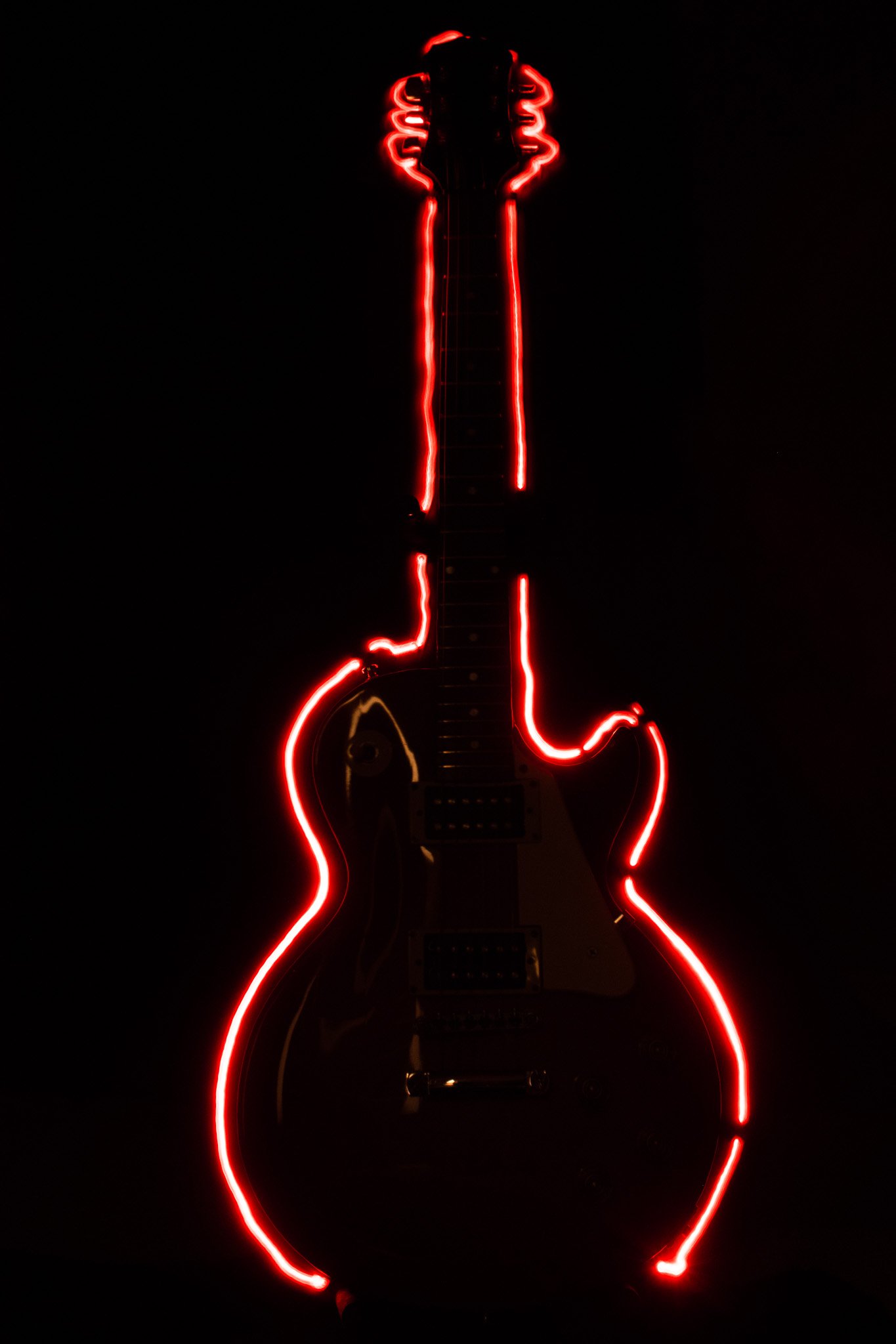 Red neon outline of an electric guitar against a black background.