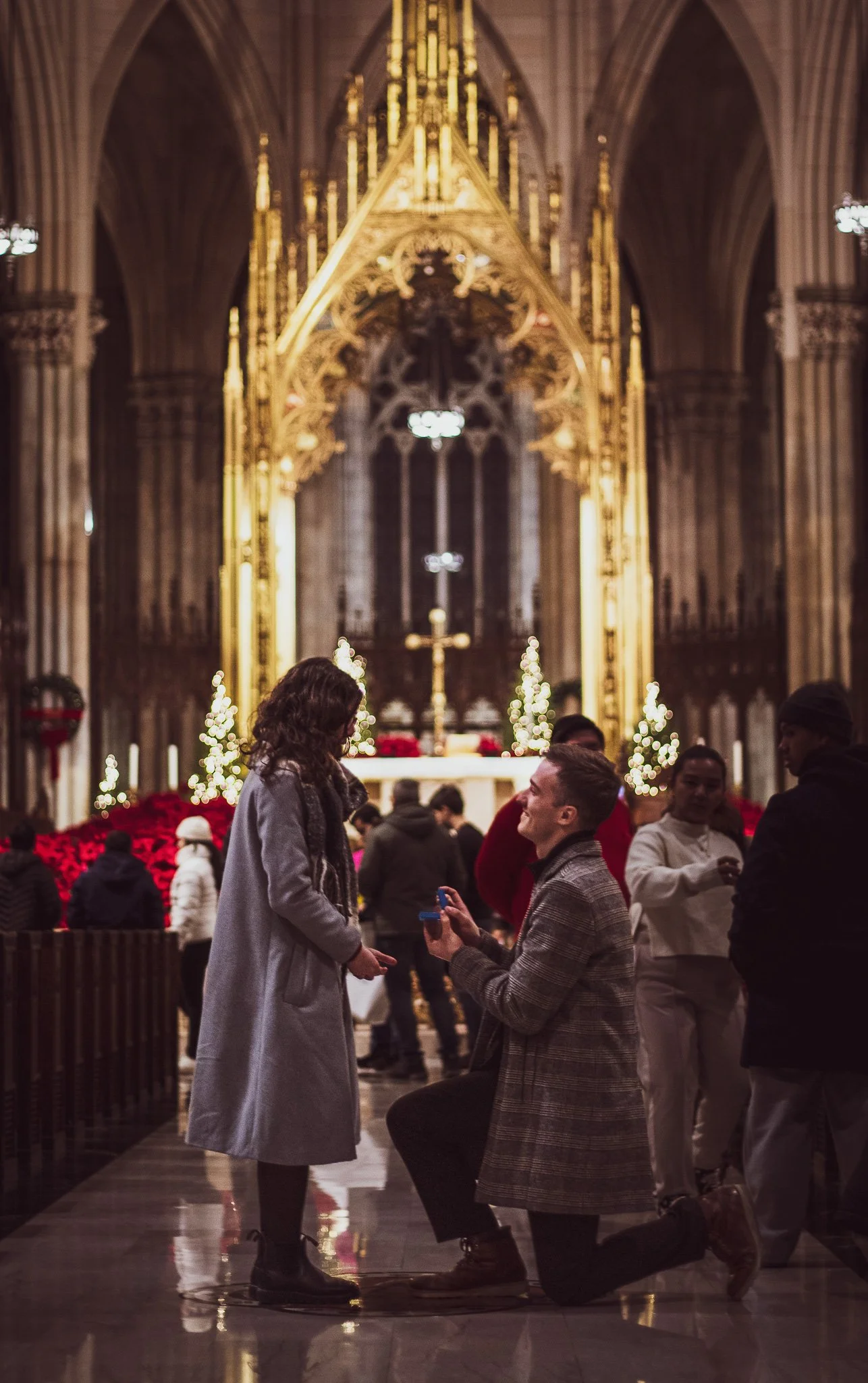 A man proposing to a woman in a church decorated for Christmas, with other people in the background.