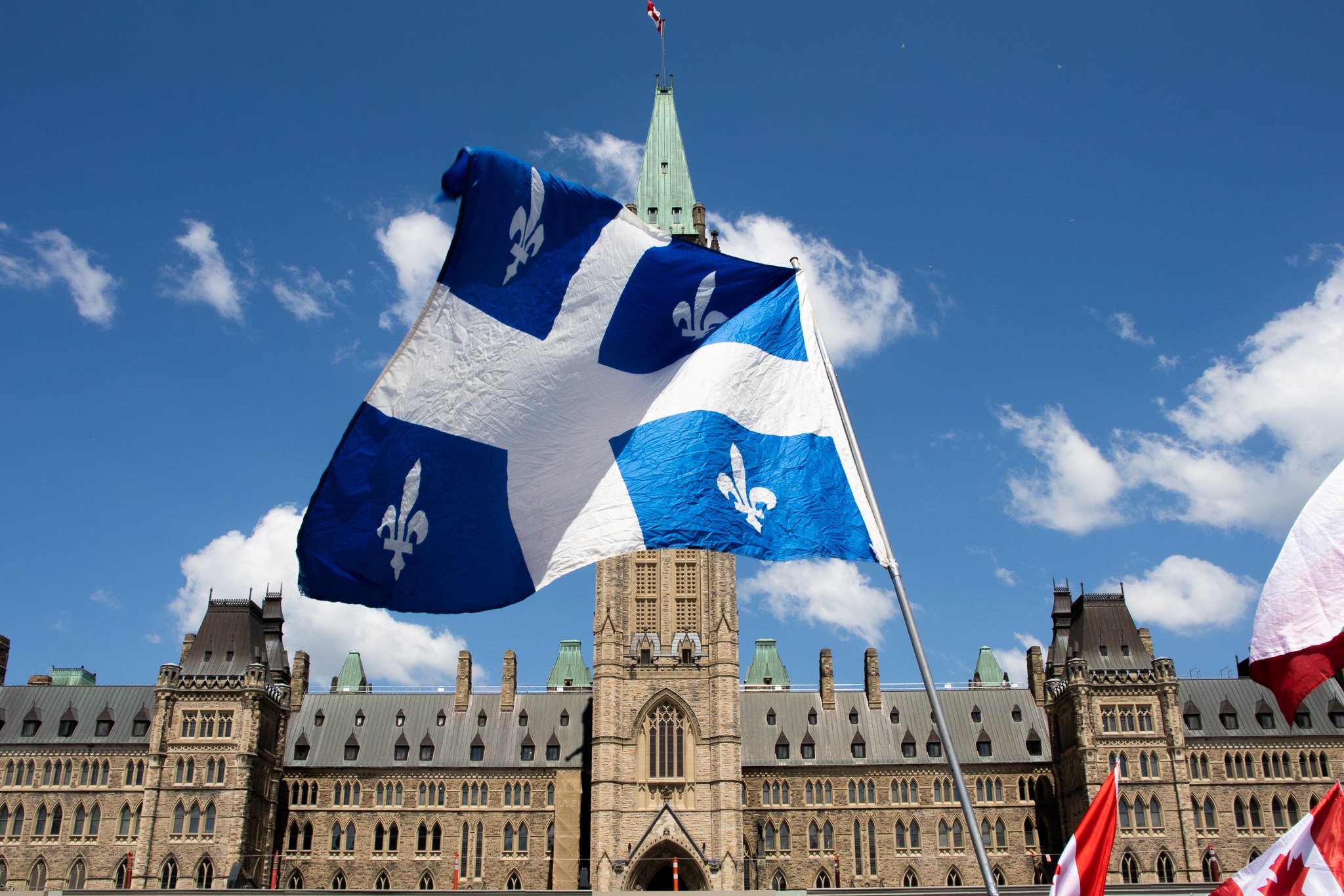 Canadian flags in front of Parliament Hill in Ottawa, with historic buildings and a clock tower in the background.
