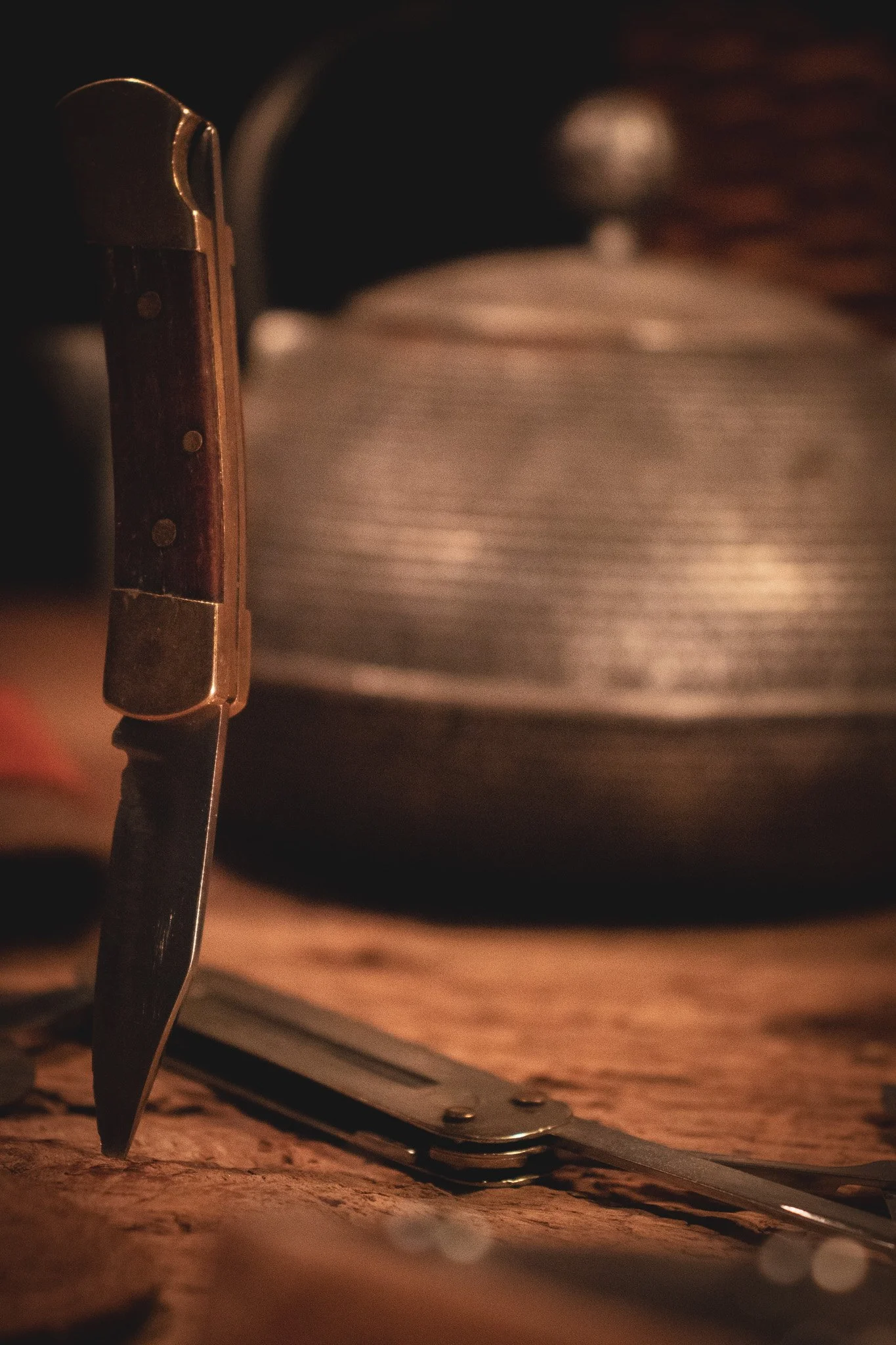 Close-up of a folding knife cutting through a piece of wood on a workbench, with a blurred background.