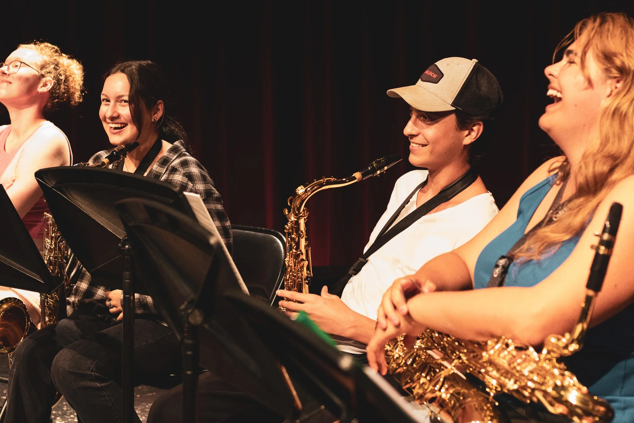 Smiling musicians sitting with their instruments during a performance or rehearsal.