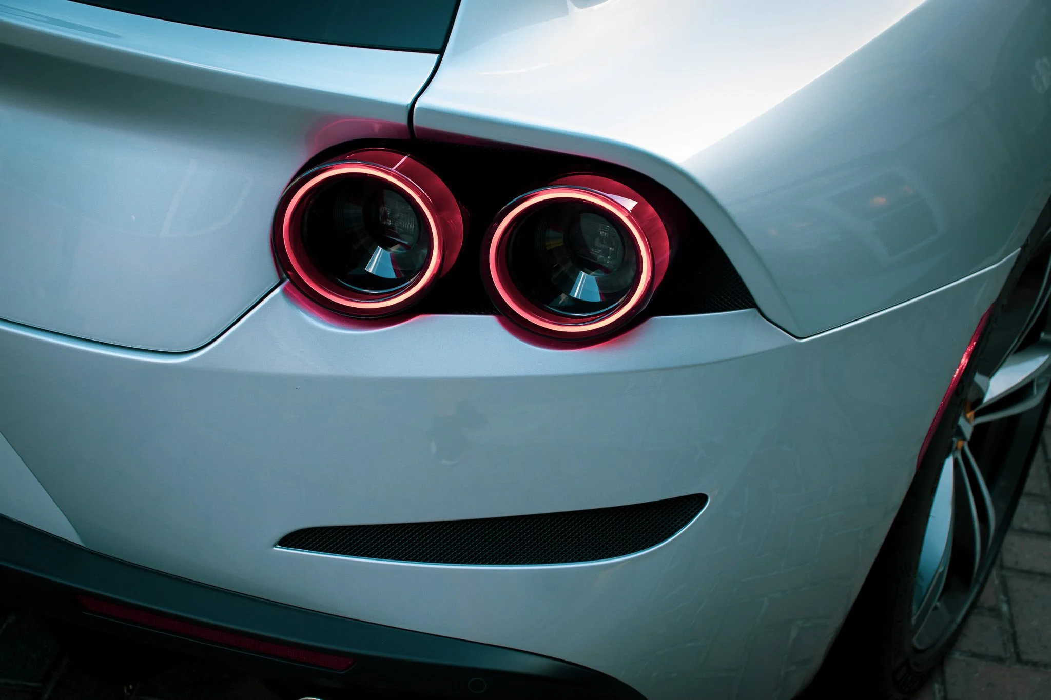 Close-up of a car's rear with illuminated red twin circular taillights and a sleek gray body.