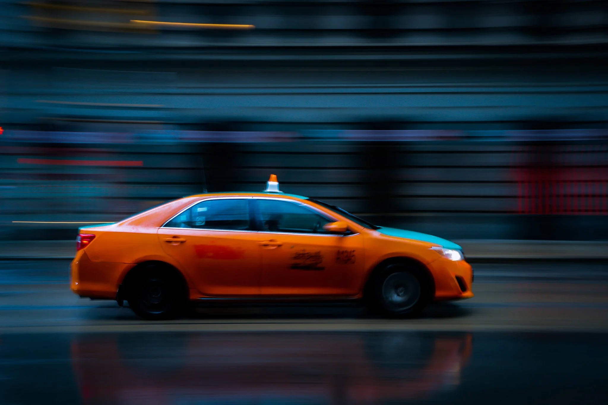 Blurred motion photo of an orange taxi cab driving through a city street at night.