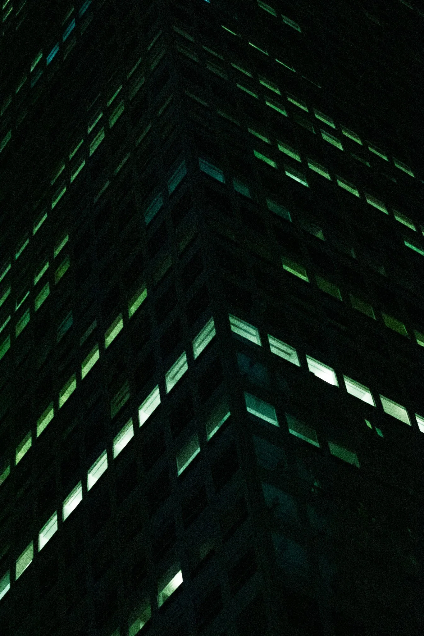 Night view of a tall building with many illuminated windows, creating a grid pattern on the dark facade.