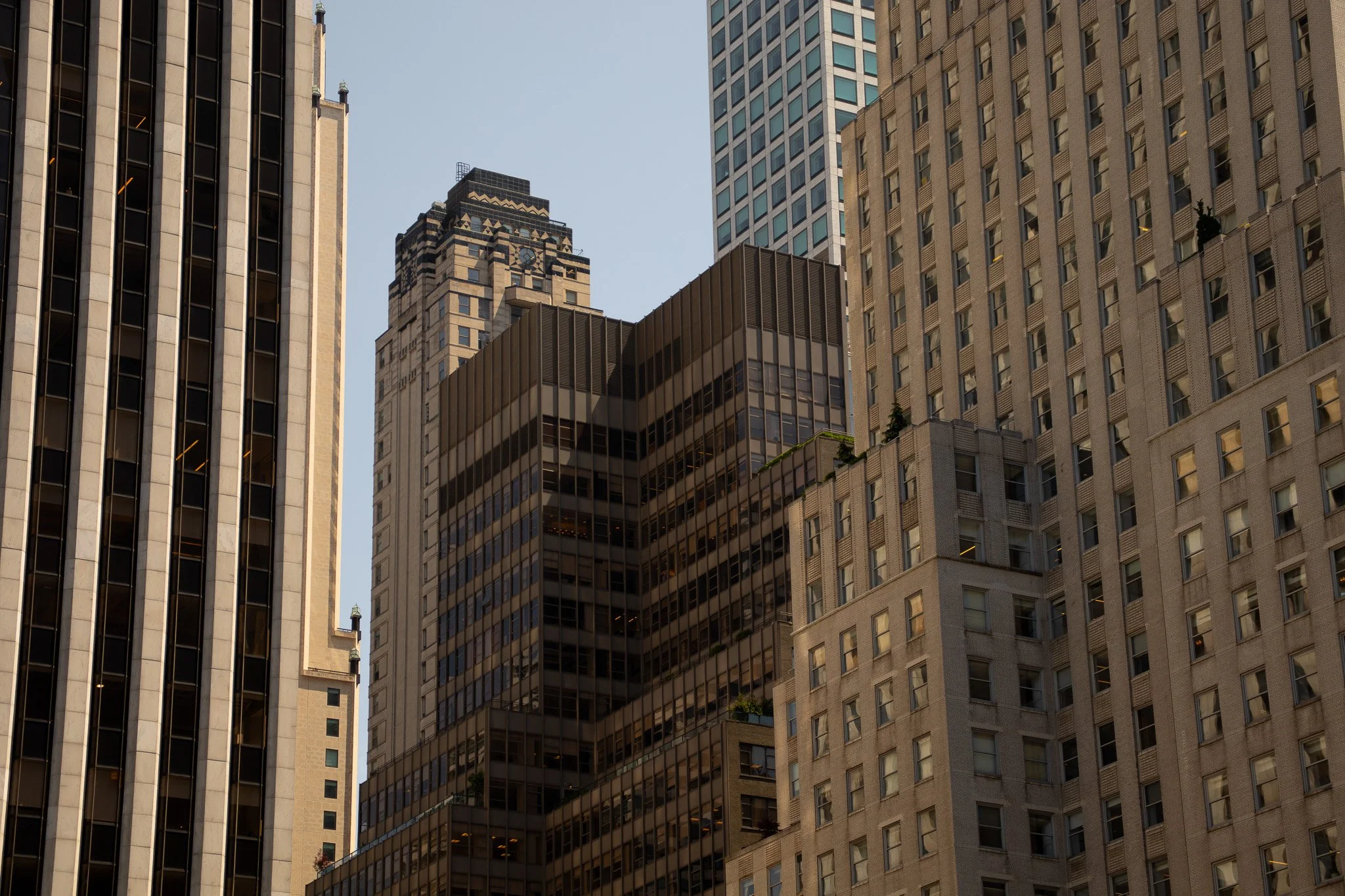 The image shows multiple tall modern skyscrapers in a city skyline, with glass windows and architectural details, under a clear blue sky.