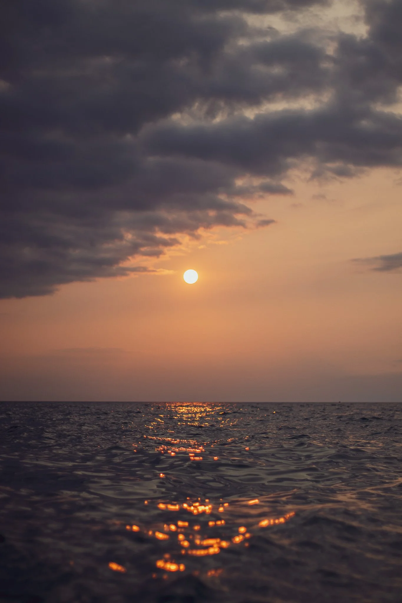 Sunset over the ocean with dark clouds in the sky and the sunlight reflecting off the water.